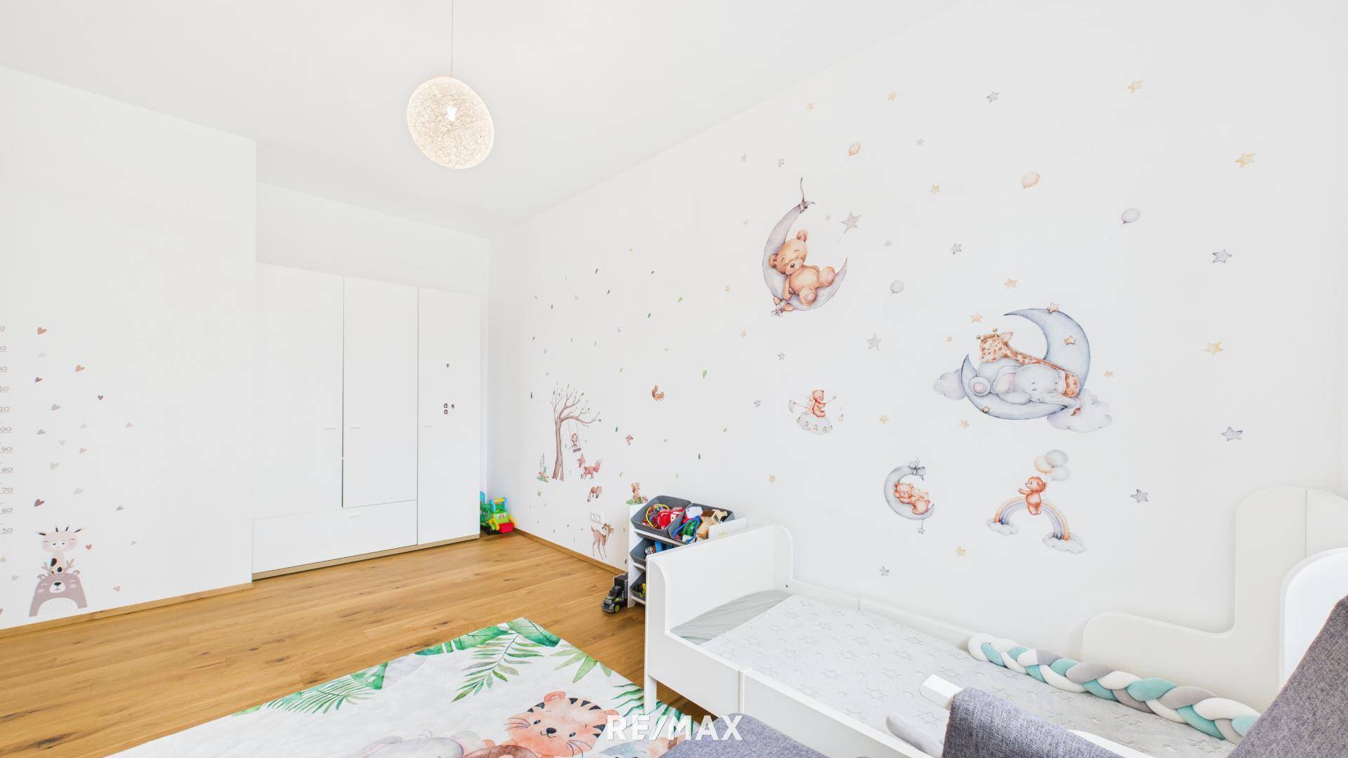 Ruhiges Kinderzimmer mit Holzboden, weißem Kleiderschrank und kindgerechter Wandgestaltung.