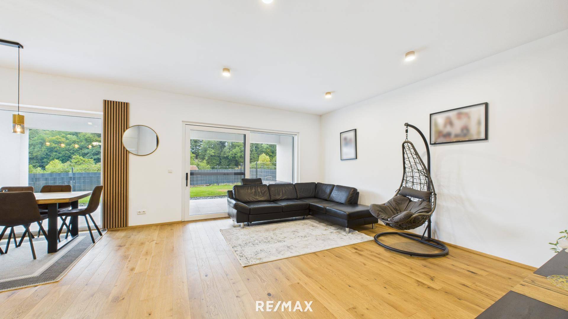 Offener Wohn- und Essbereich mit Holzboden, Ledersofa und Zugang zur Terrasse mit Gartenblick.