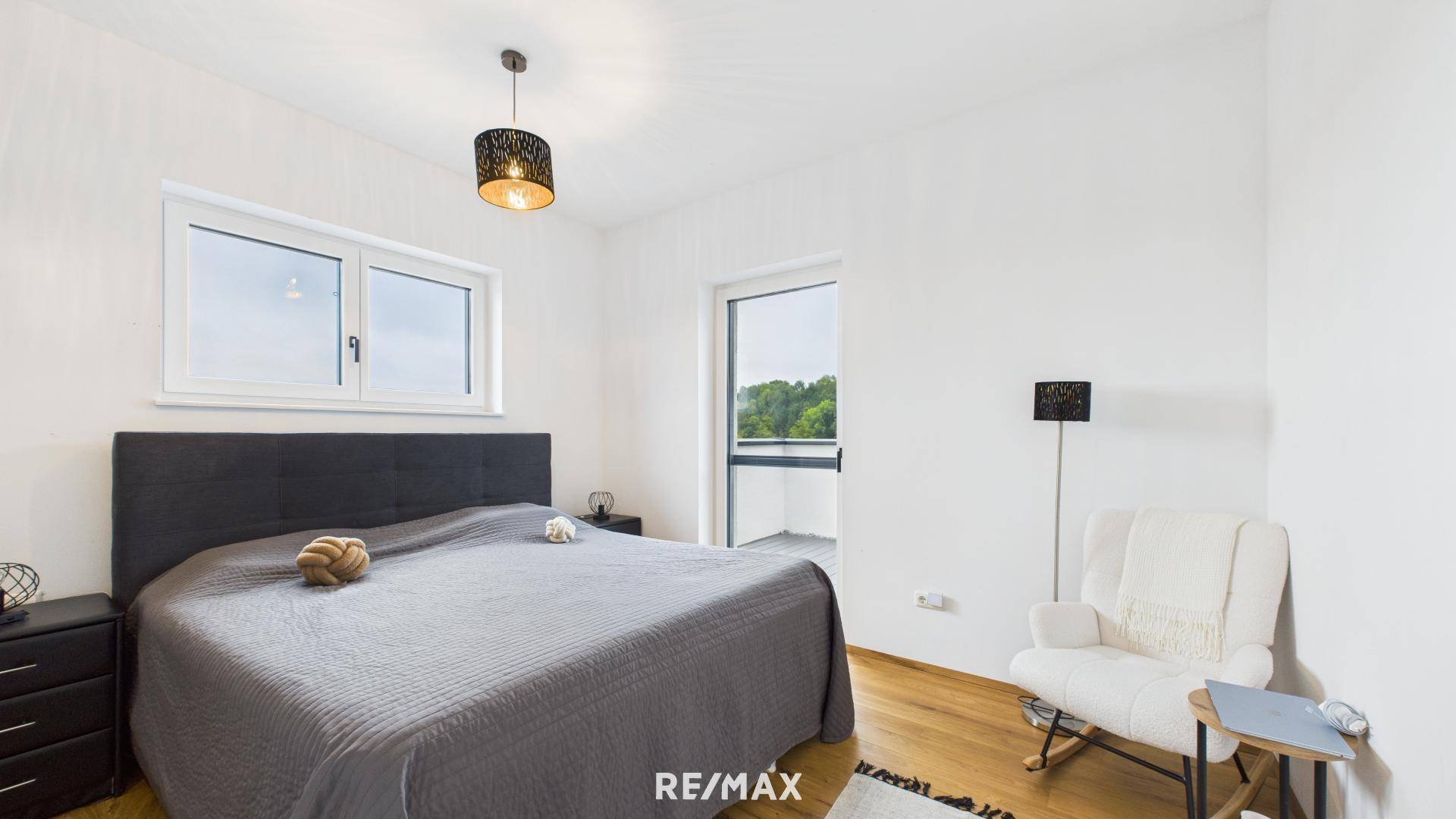 Helles Schlafzimmer mit Doppelbett, Holzboden und Zugang zu einem Balkon mit grüner Aussicht.
