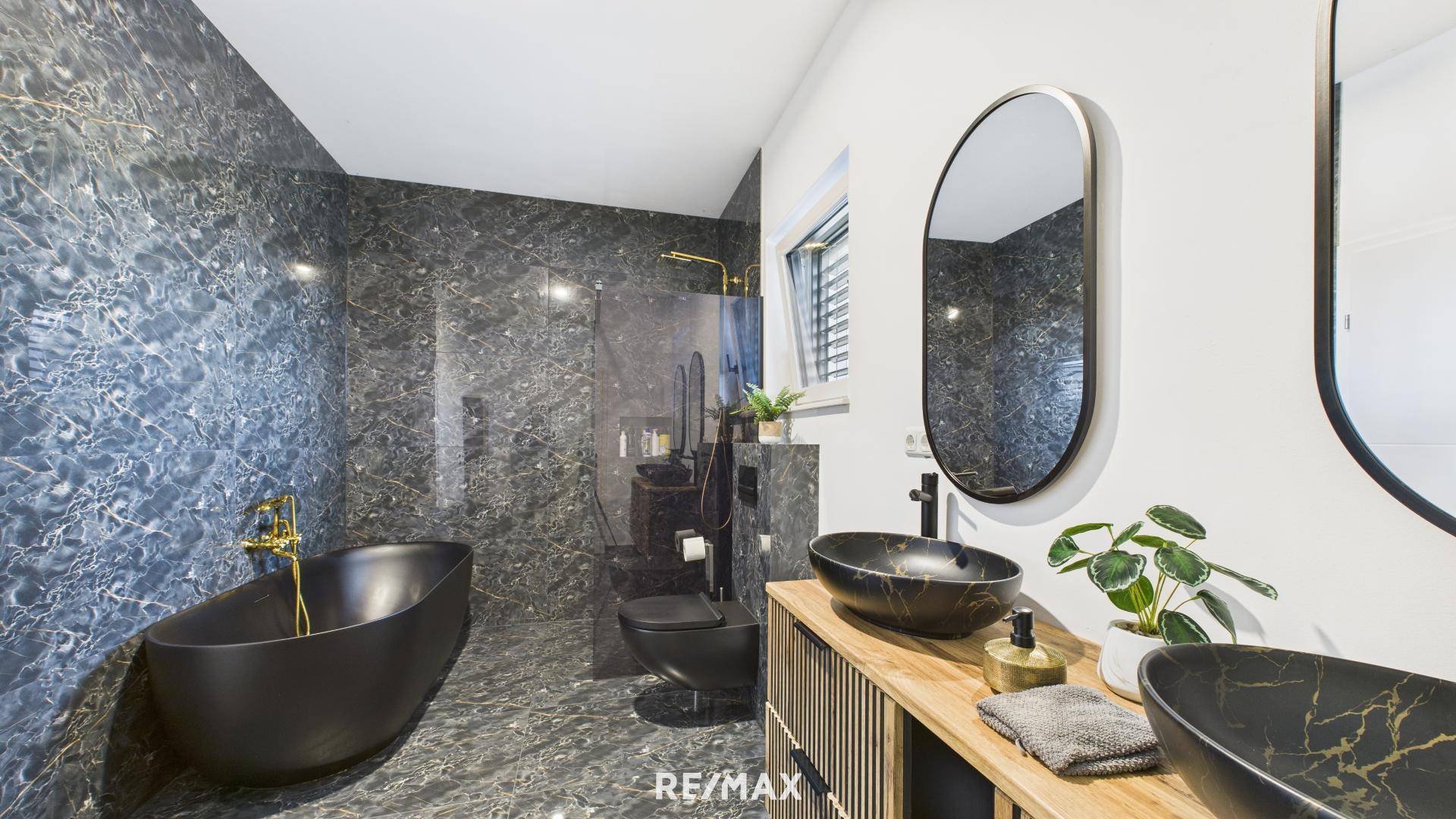 Luxuriöses Badezimmer mit dunklen Marmorfliesen, freistehender Badewanne und Doppelwaschbecken.