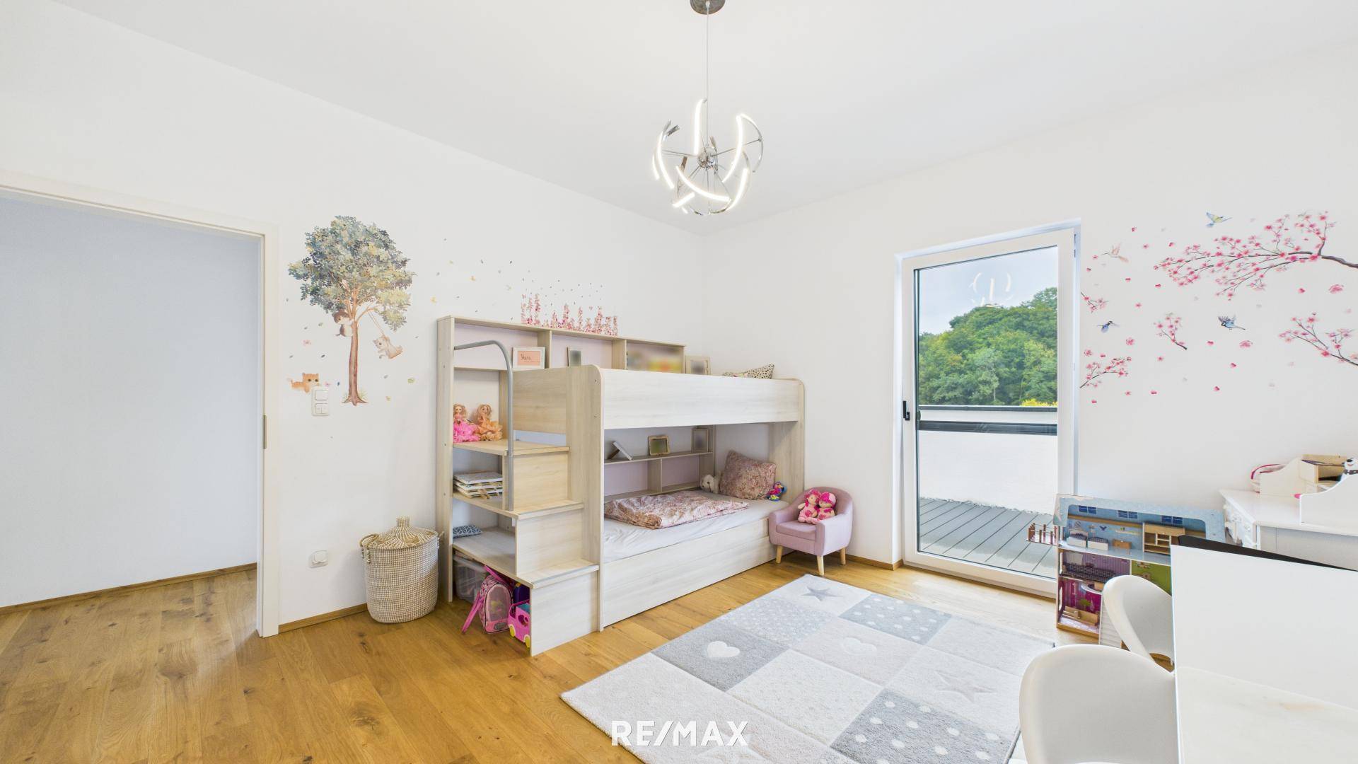 Helles Kinderzimmer mit Etagenbett, Schreibtisch und Zugang zu einem kleinen Balkon.