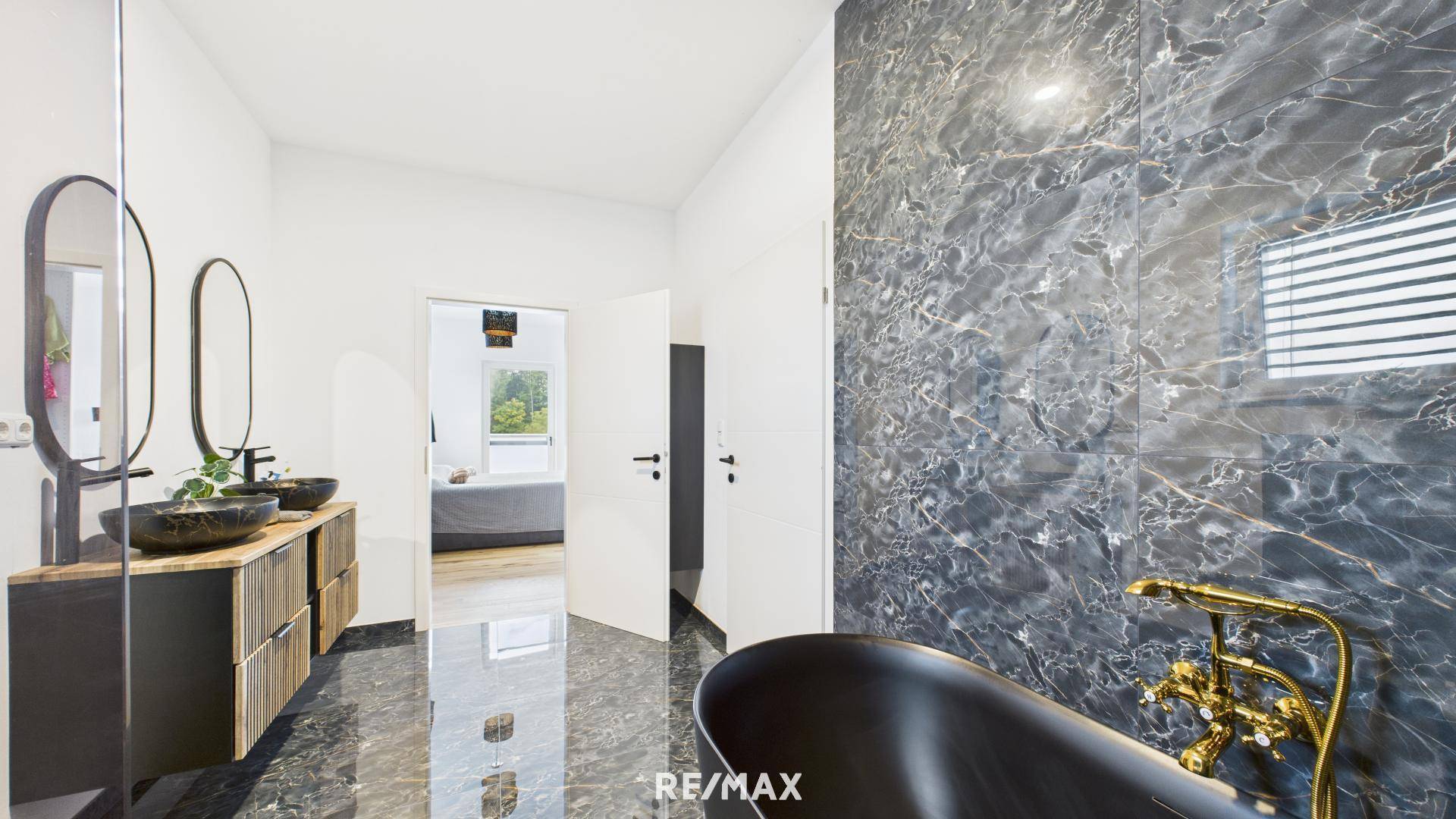 Elegantes Badezimmer mit dunklen Marmorfliesen und Blick durch die offene Tür ins Schlafzimmer.
