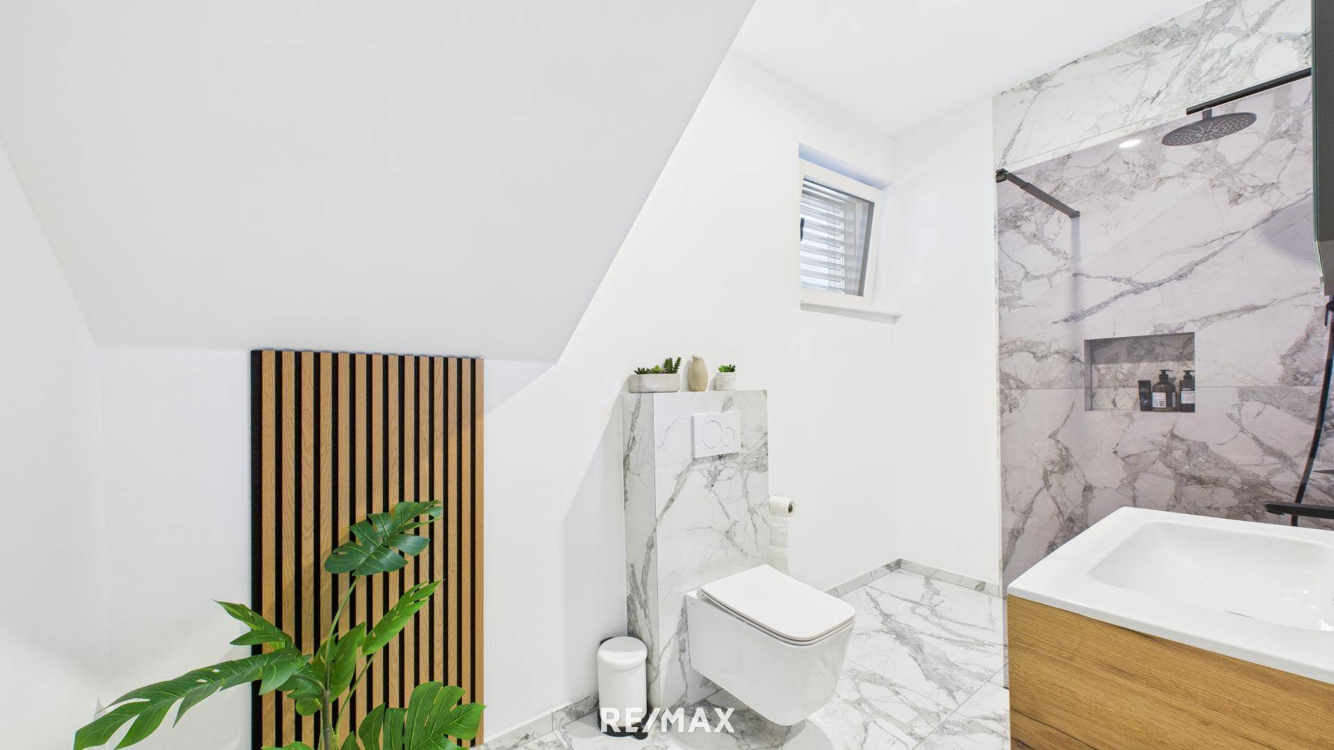 Modernes Badezimmer mit Marmorfliesen, wandhängendem WC und begehbarer Dusche unter Dachschräge.
