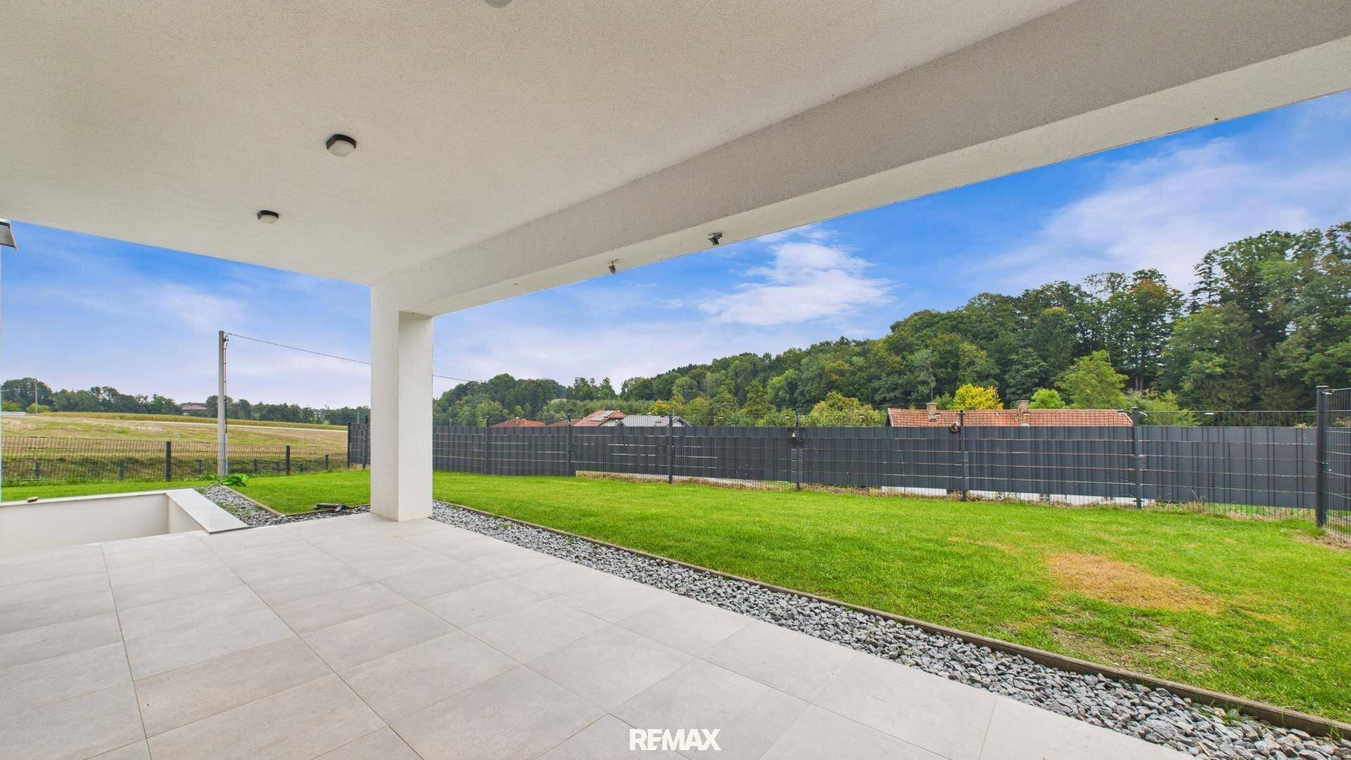 Überdachte Terrasse mit modernen Fliesen und direktem Zugang zum grünen Gartenbereich.