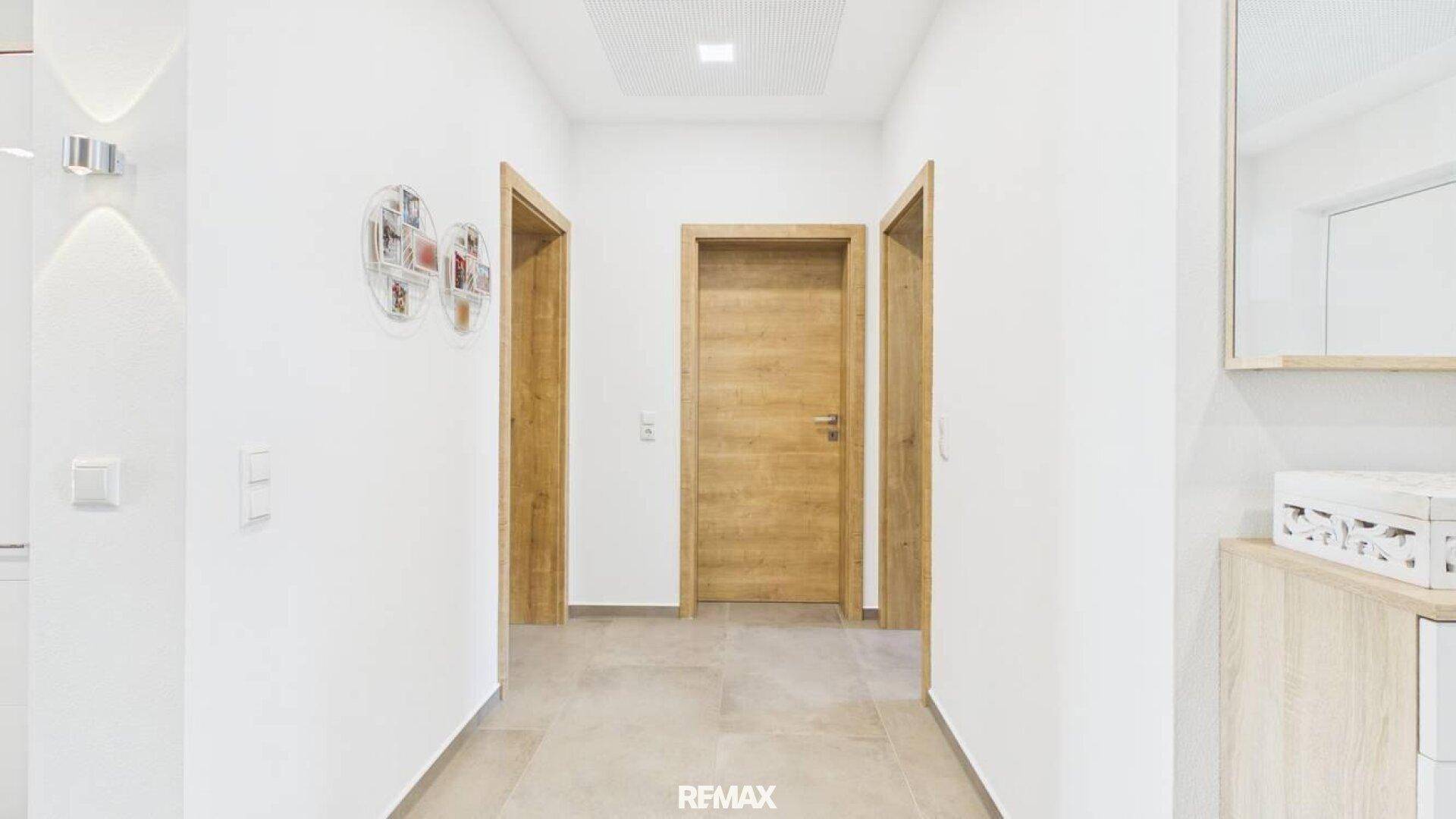 Heller Flur mit drei Holztüren, weißen Wänden und modernem Fliesenboden.