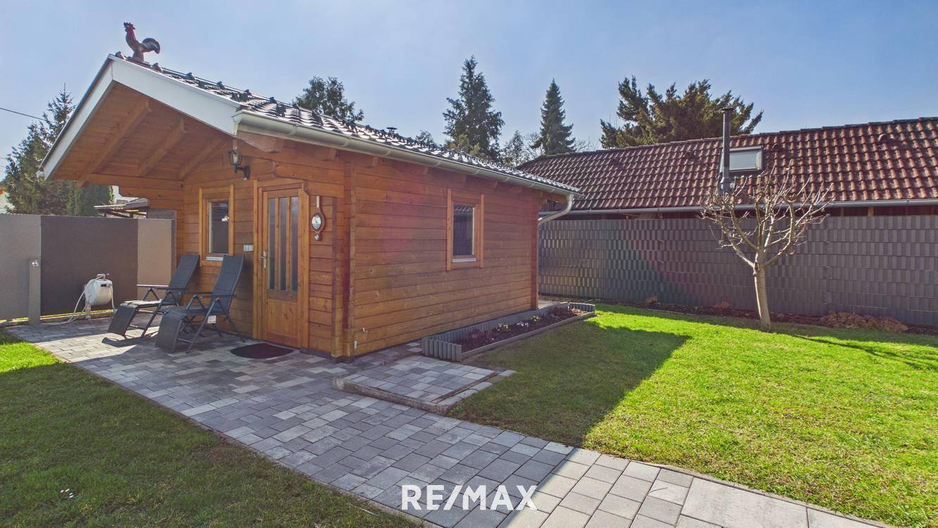 Charmantes Holzhaus im Garten mit gepflastertem Weg und gepflegtem Rasenbereich.