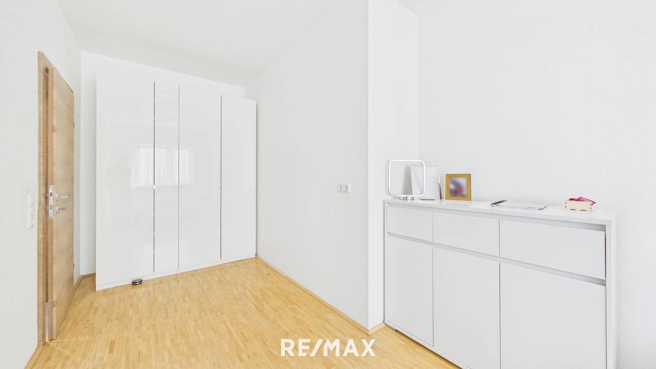 Helles Schlafzimmer mit weißem Kleiderschrank, Holzboden und viel Tageslicht.