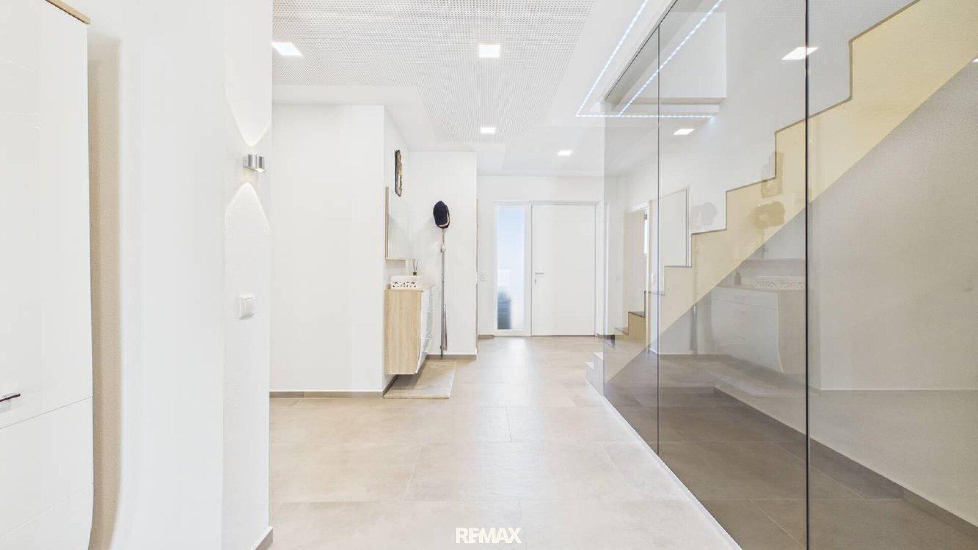 Heller Flur mit moderner Glaswand neben der Treppe und hellem Fliesenboden.