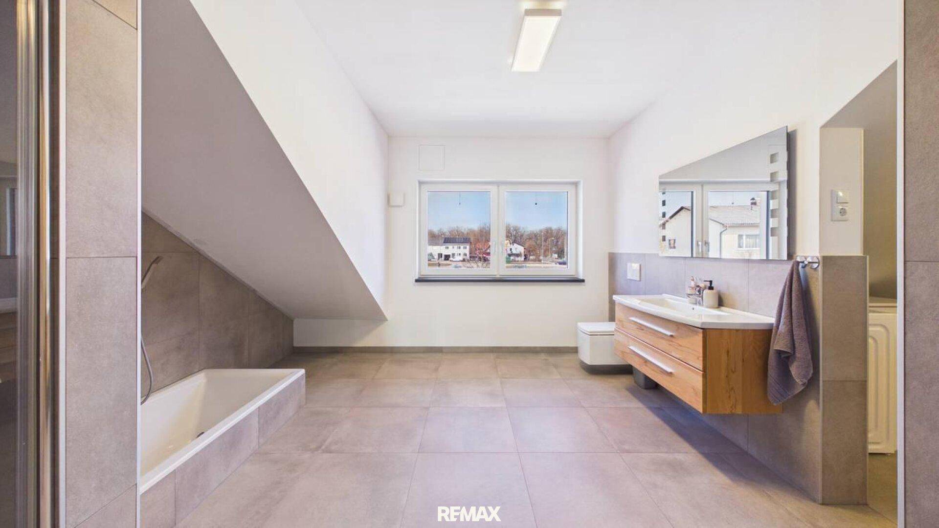 Modernes Badezimmer mit Badewanne, Waschtisch und Fenster unter einer Dachschräge.