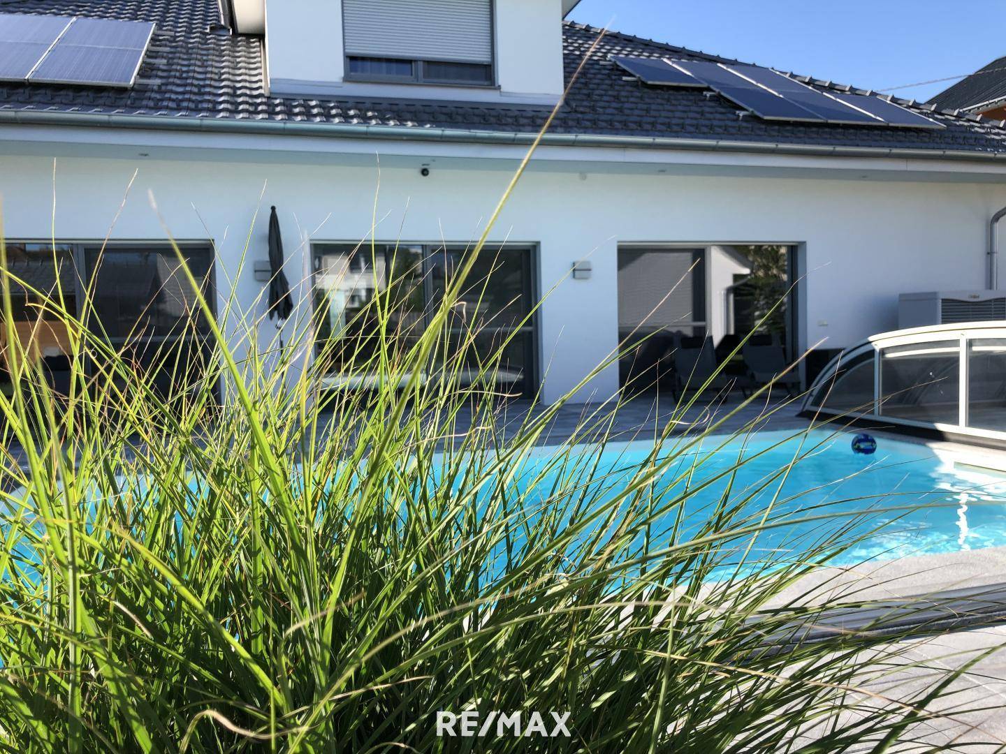 Außenansicht des Hauses mit Swimmingpool und Solaranlagen auf dem Dach an einem sonnigen Tag.