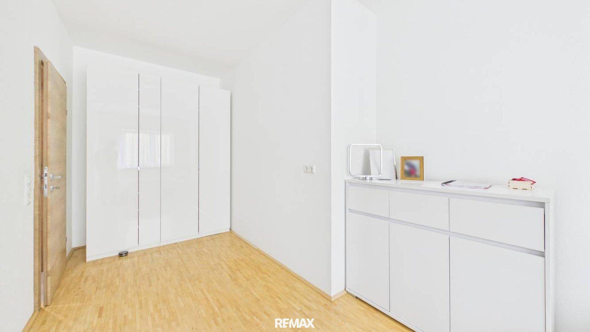 Helles Zimmer mit weißem Kleiderschrank, Kommode und hellem Holzfußboden.