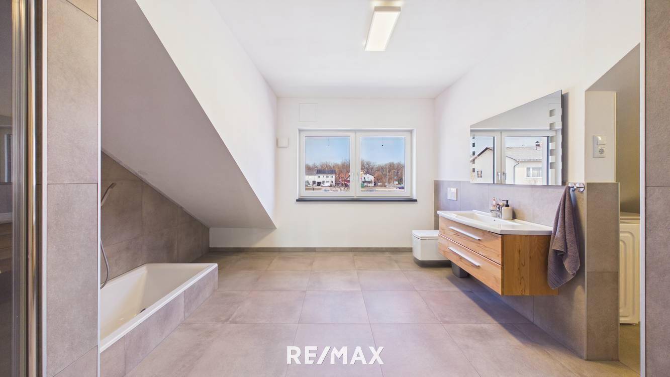 Modernes Badezimmer mit Badewanne, schwebendem Waschtisch, WC und Fenster unter Dachschräge.