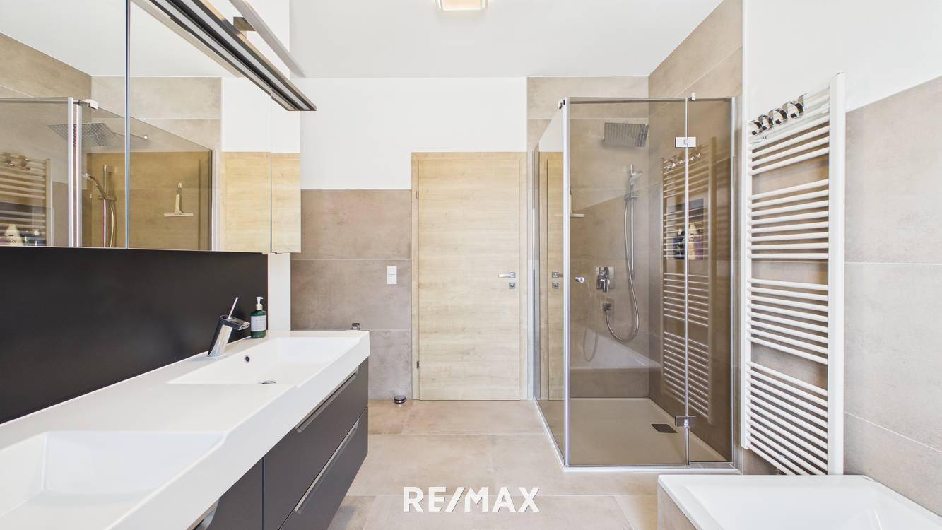 Elegantes Badezimmer mit großer Duschkabine, Doppelwaschbecken und beheiztem Handtuchhalter.