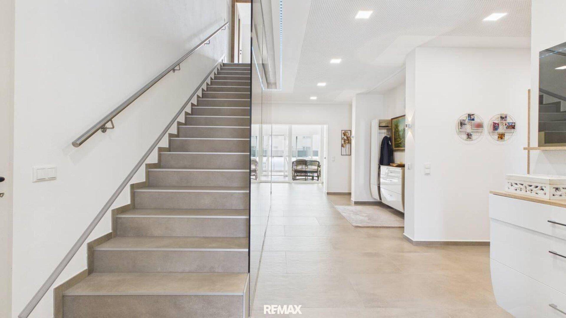 Moderner Eingangsbereich mit eleganter Treppe, Glasgeländer und hellem Fliesenboden.