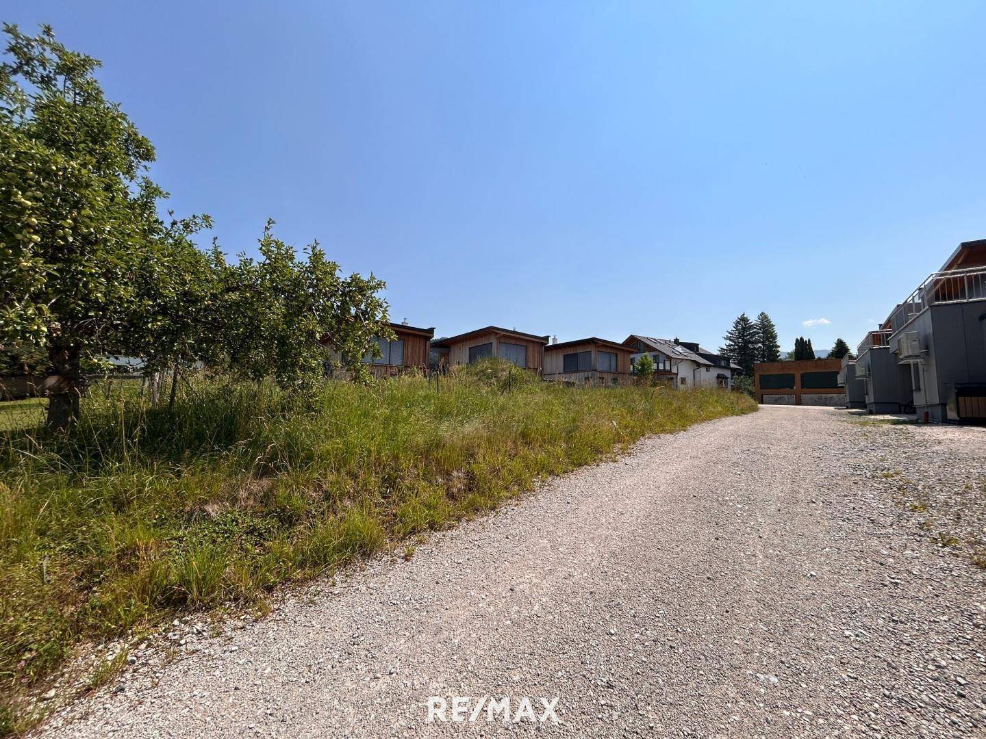 Kiesweg führt zu modernen Häusern mit Holzfassaden und großen Fenstern in ländlicher Umgebung.