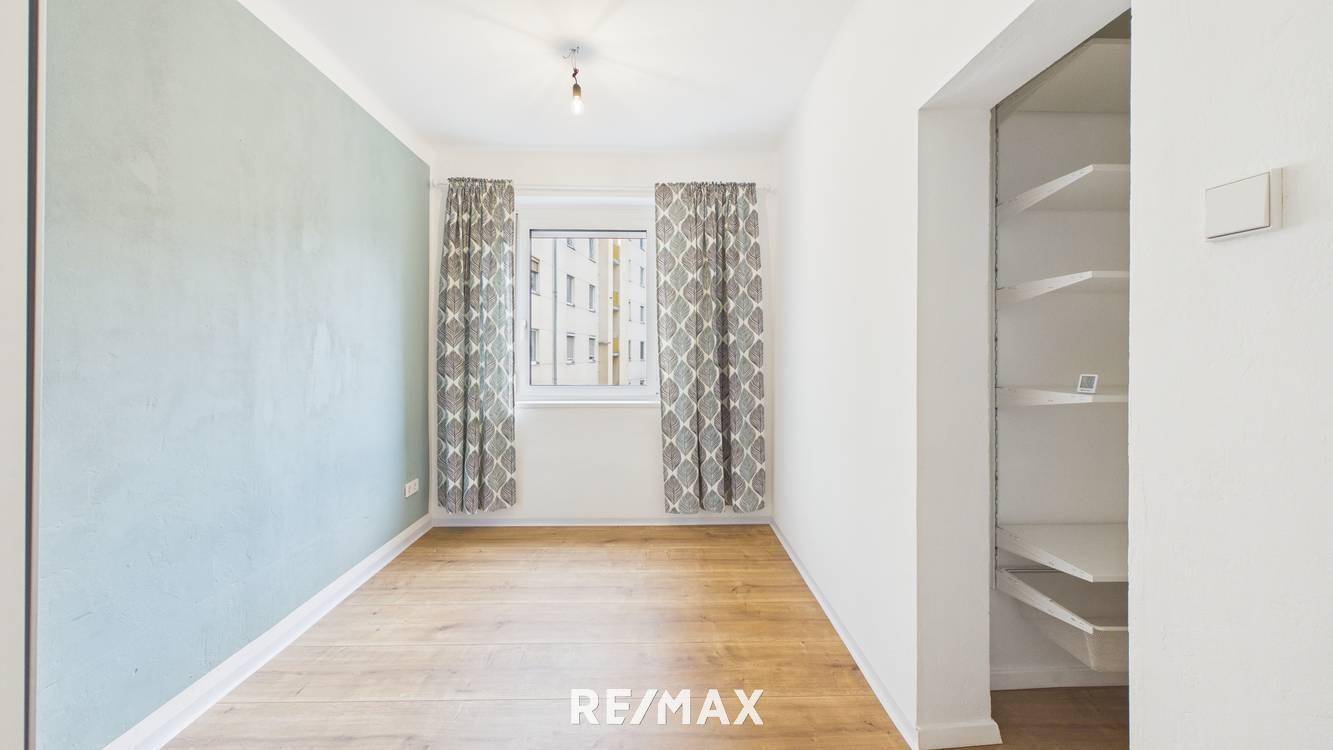 Helles Zimmer mit Holzboden, einer blaugrauen Akzentwand und integrierten Regalen.