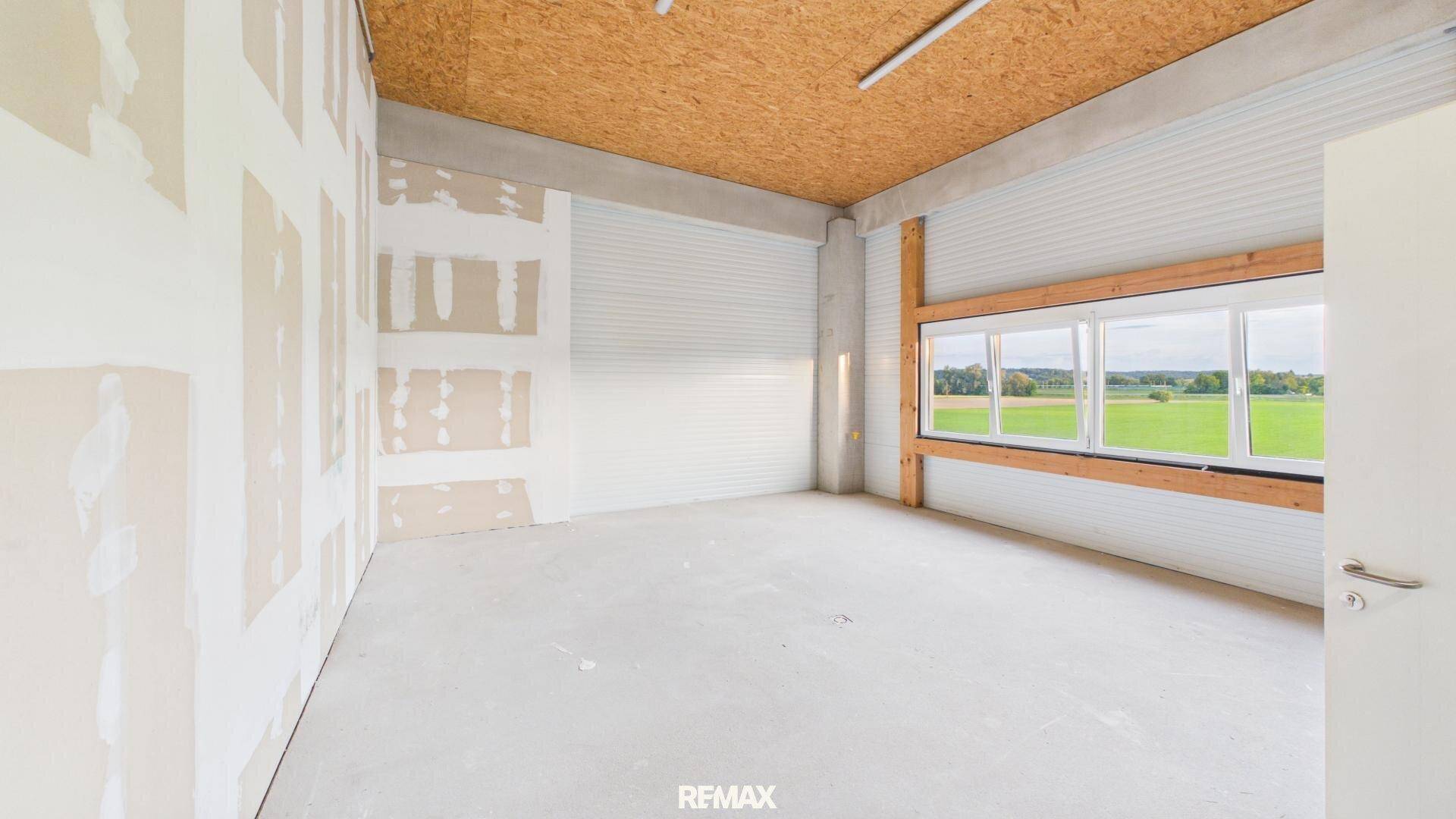 Unfertiger Büroraum mit großen Fenstern, Blick ins Grüne und Holzdecke, bereit für den Innenausbau.