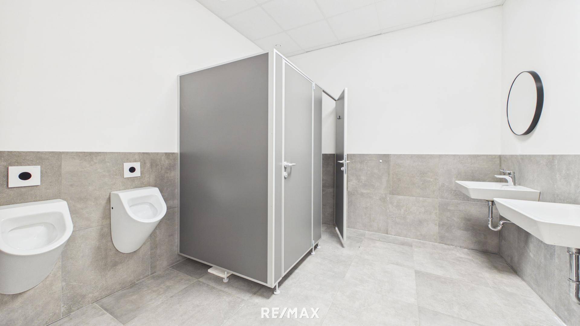 Moderne Toilettenanlage mit Urinal, Kabinen und Waschbecken, in neutralen Farben gehalten.