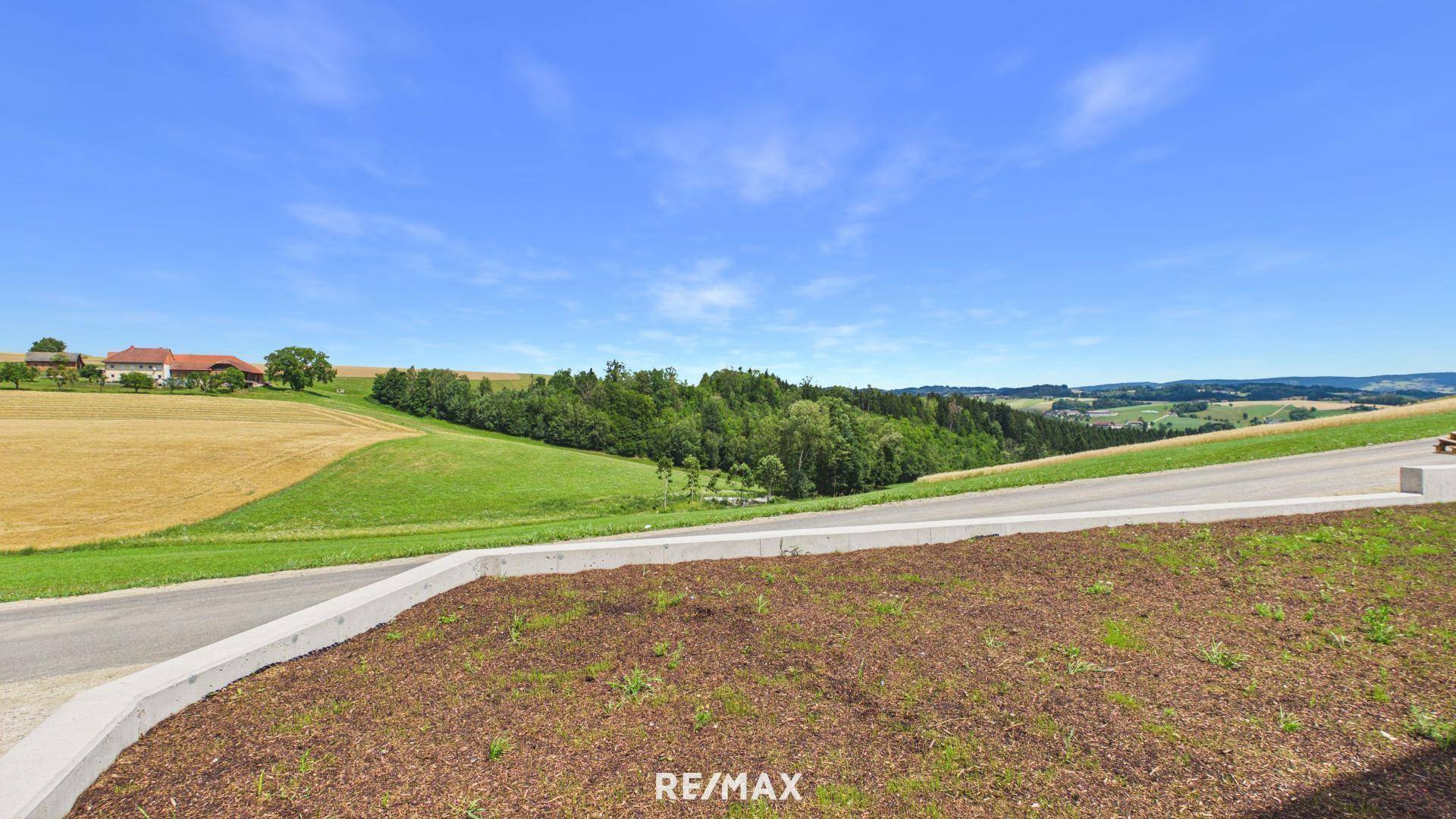 Unbebautes Grundstück mit Blick auf die weite, grüne Landschaft und ferne Häuser.