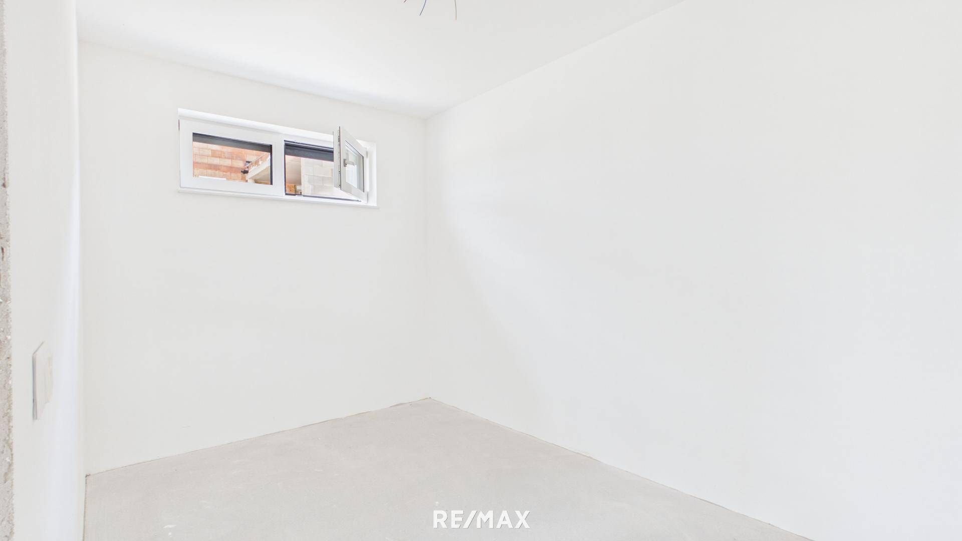 Helles Schlafzimmer im Rohbau mit Fenster und Blick auf die Umgebung.