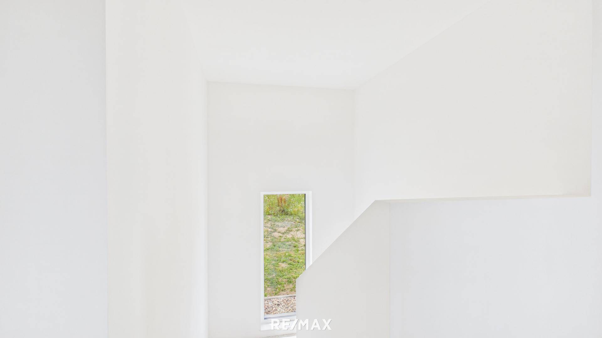 Treppenhausbereich im Rohbau mit hohem Fenster, das viel Tageslicht hereinlässt.