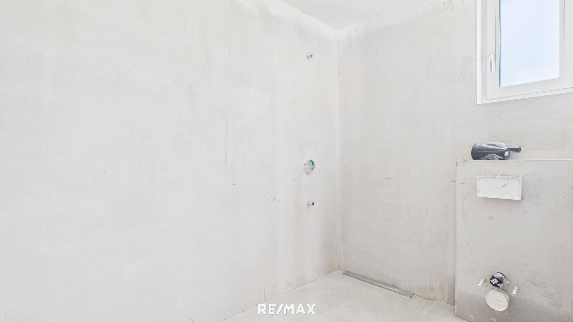 Badezimmer im Rohbau mit Fenster und vorbereiteten Anschlüssen für Sanitärinstallationen.