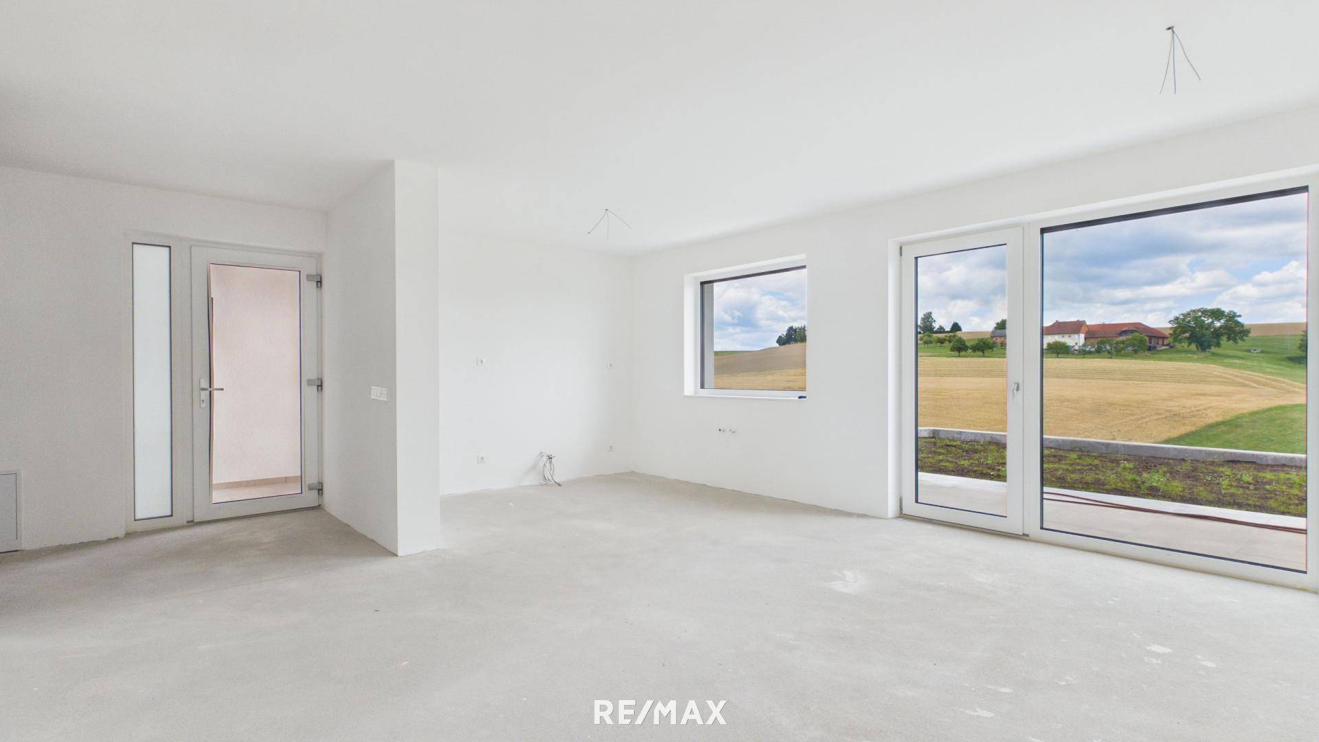 Lichtdurchfluteter Raum im Rohbau mit großen Fenstern und Zugang zum Außenbereich.