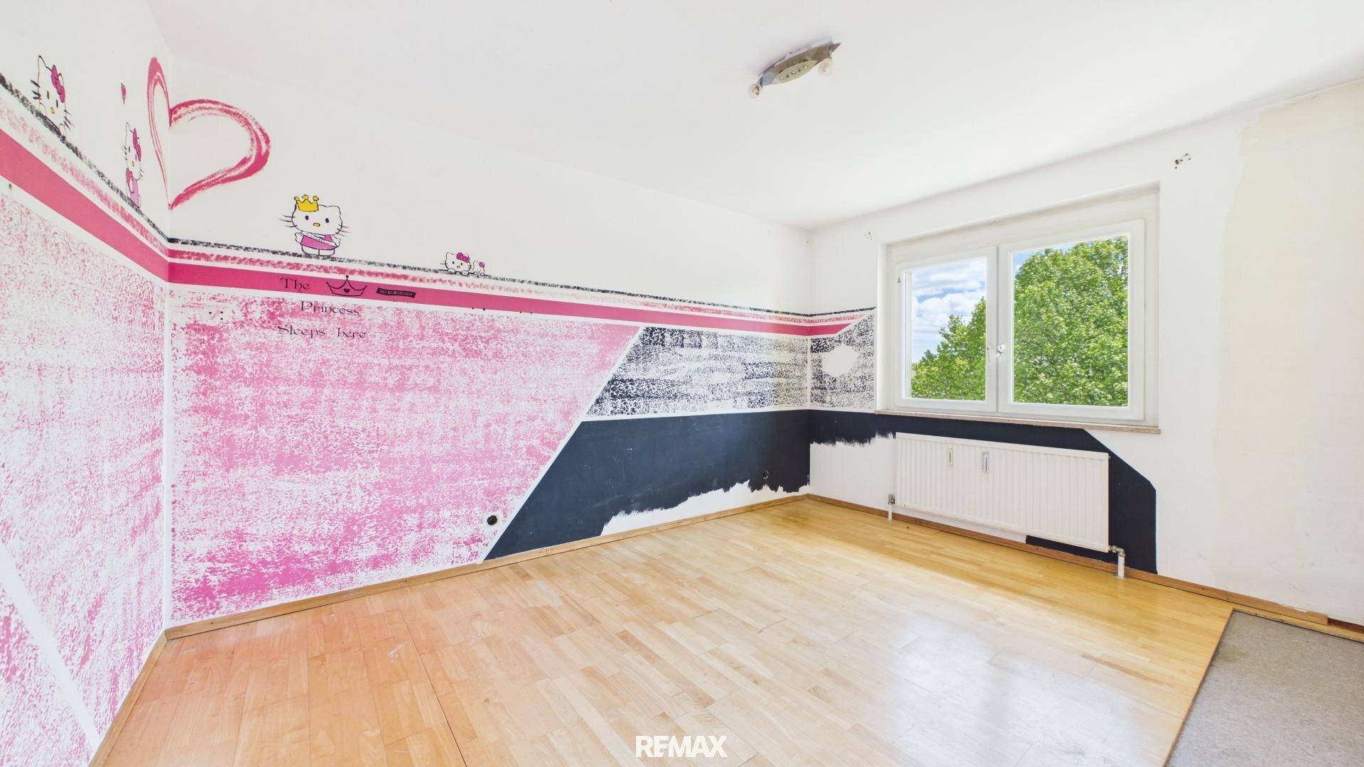 Kinderzimmer mit farbenfrohen rosa-schwarzen Wänden, Holzboden und Blick ins Grüne.