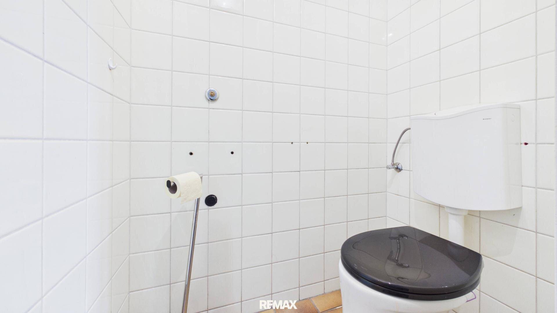 Separates WC mit weißen Wandfliesen und einer Toilette mit dunklem Sitz.