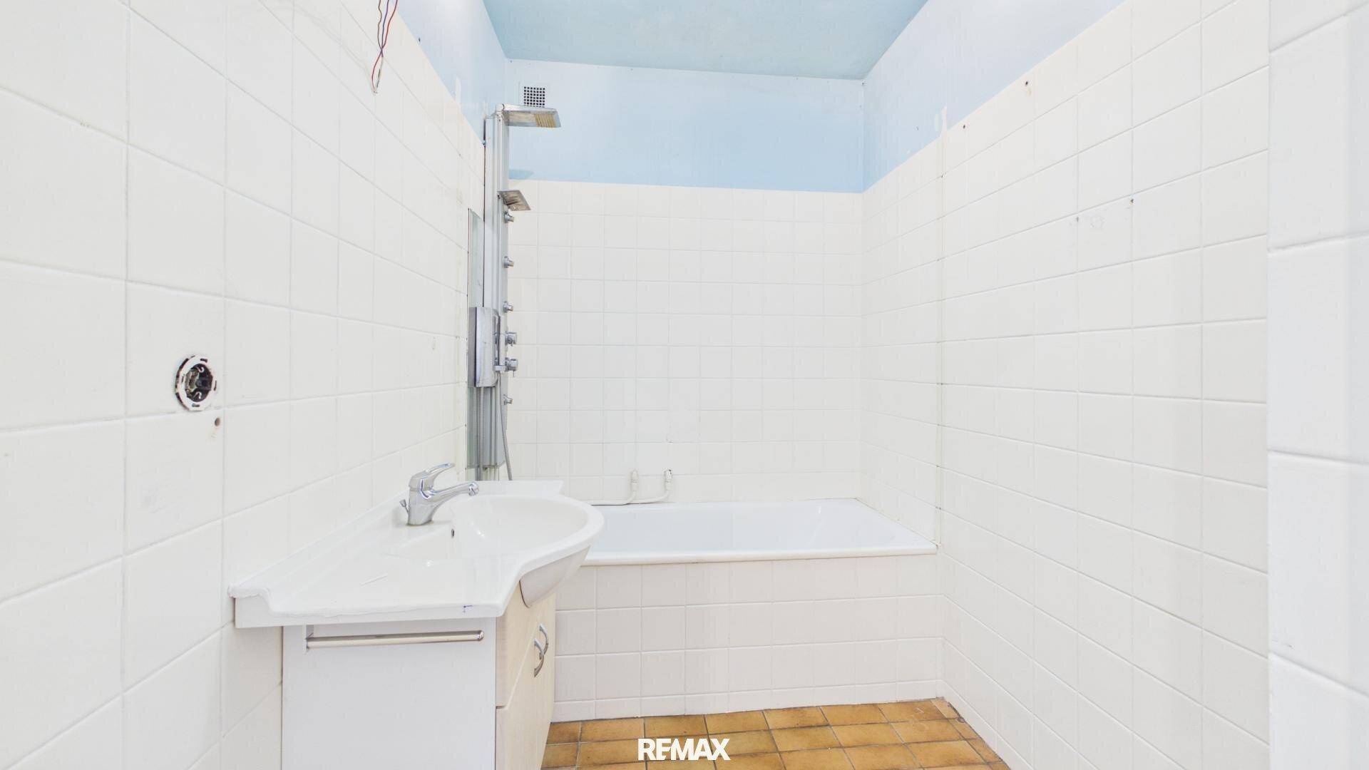 Badezimmer mit weißen Wandfliesen, Badewanne, Dusche und einem Waschbecken mit Unterschrank.
