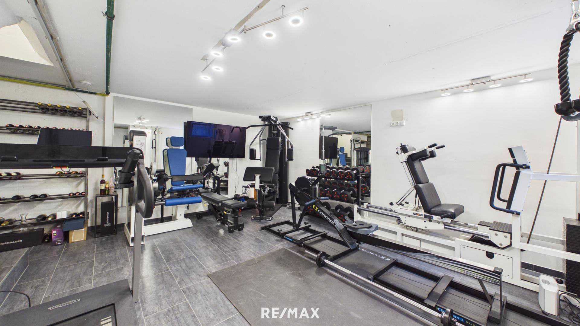 Gut ausgestatteter Fitnessraum mit verschiedenen Trainingsgeräten und Spiegeln.