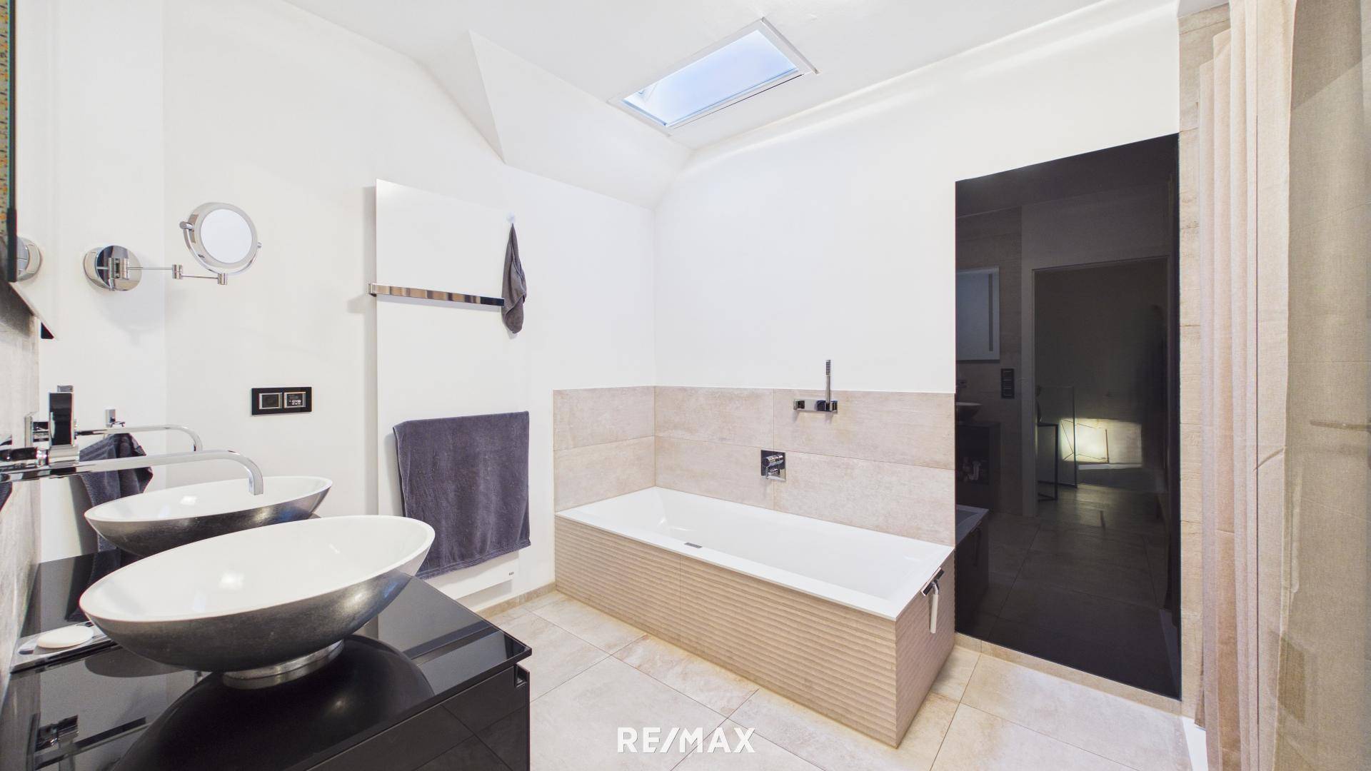 Modernes Badezimmer mit Badewanne, Doppelwaschbecken und natürlichem Licht durch ein Dachfenster.