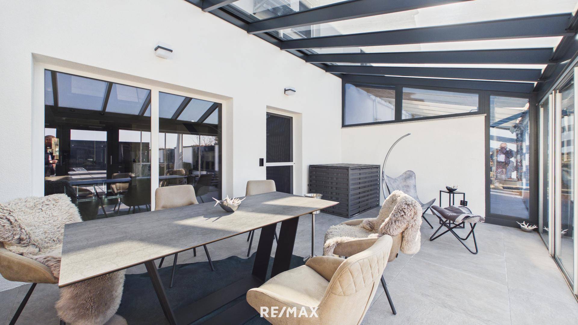 Überdachte Terrasse mit großem Esstisch und modernen Stühlen, ideal für Mahlzeiten im Freien.