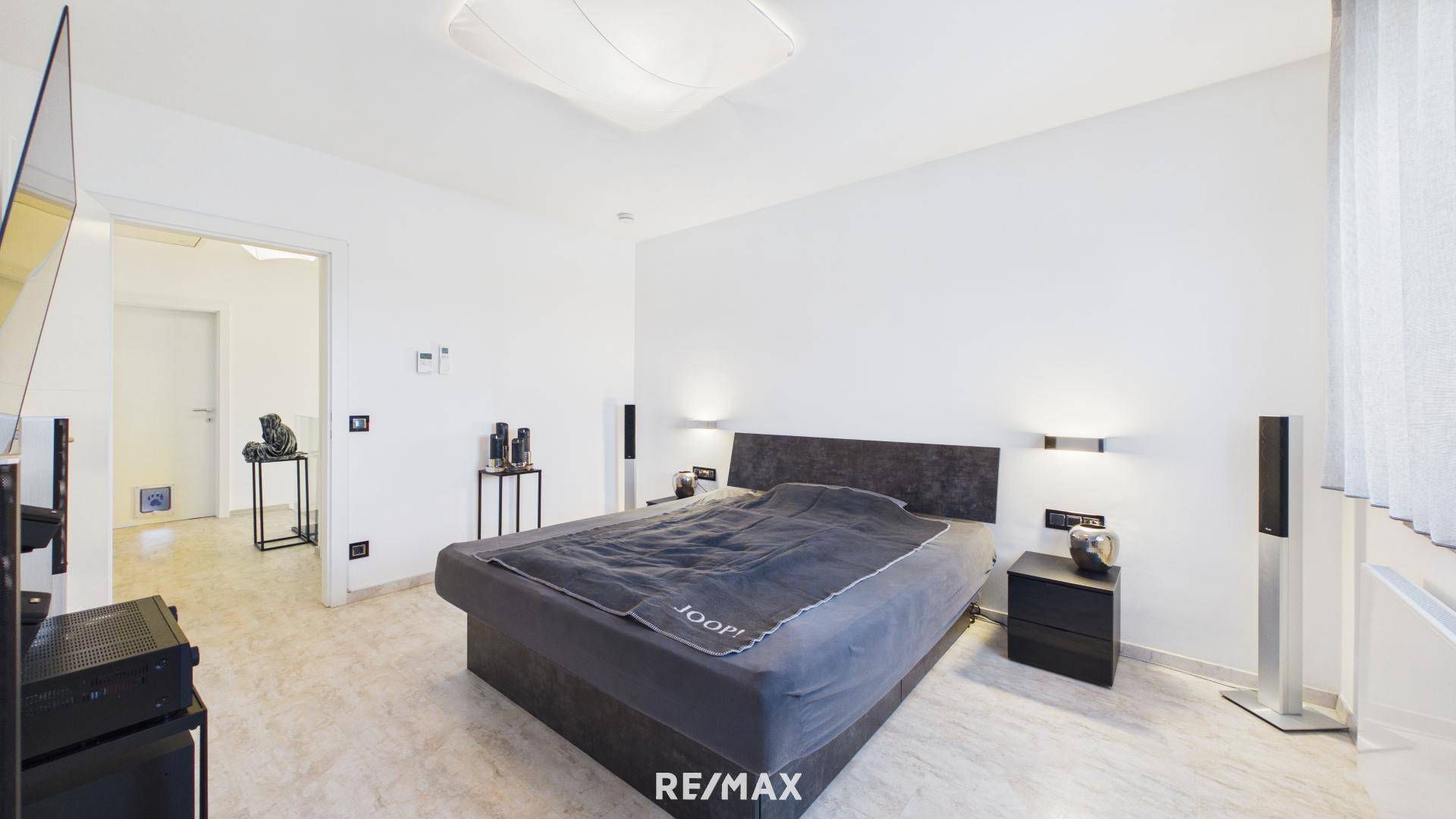 Helles Schlafzimmer mit großem Bett, minimalistischer Einrichtung und Steinboden.