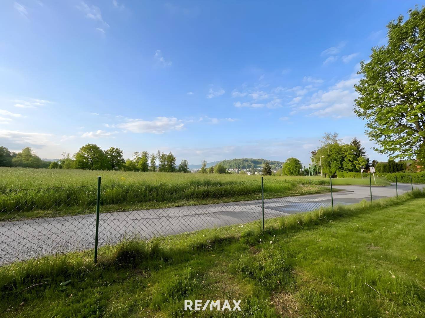 Panoramablick über weite grüne Felder und eine Straße mit Hügeln in der Ferne.