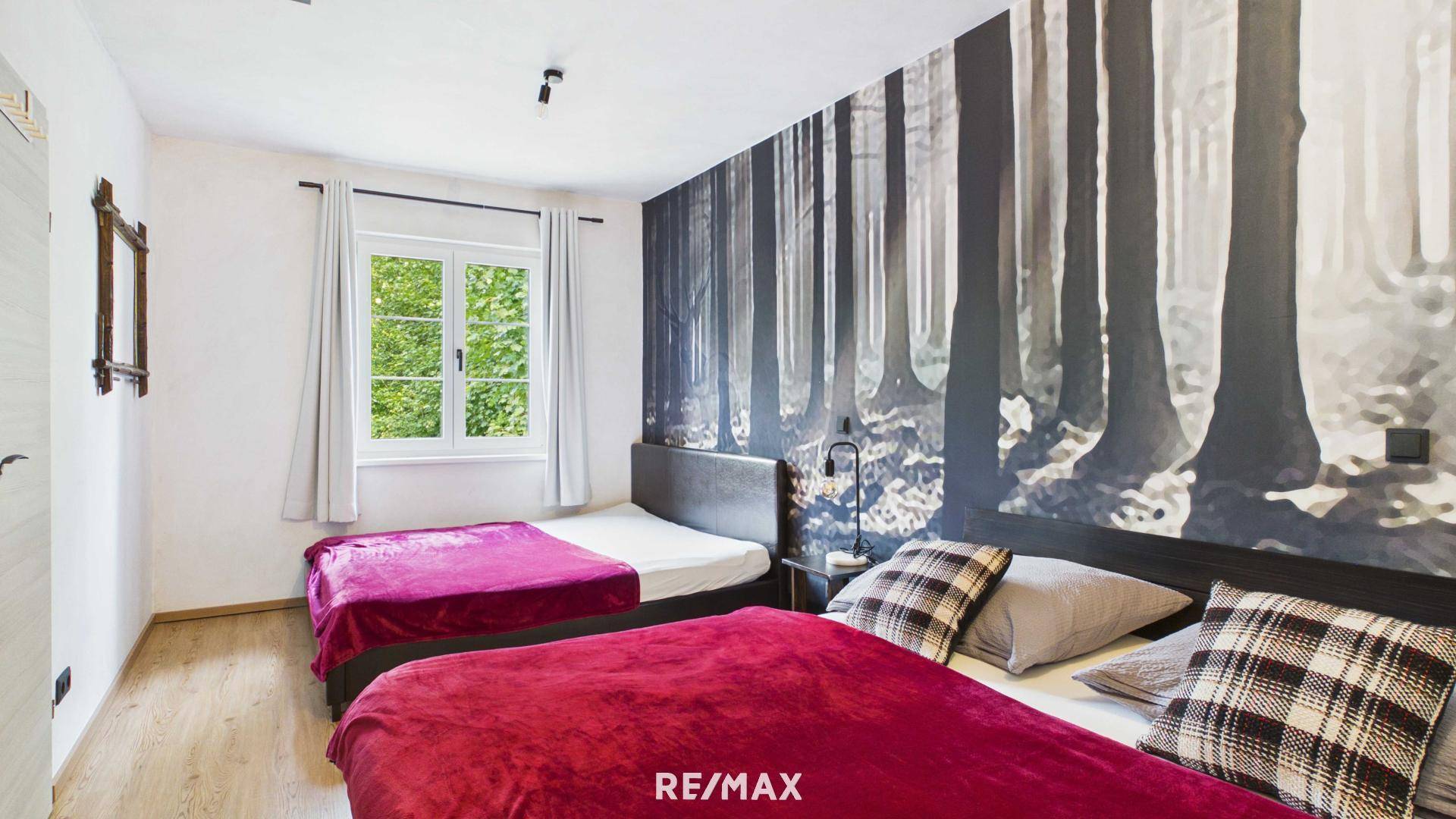 Gemütliches Schlafzimmer mit zwei Betten und einer Waldtapete als Akzentwand.