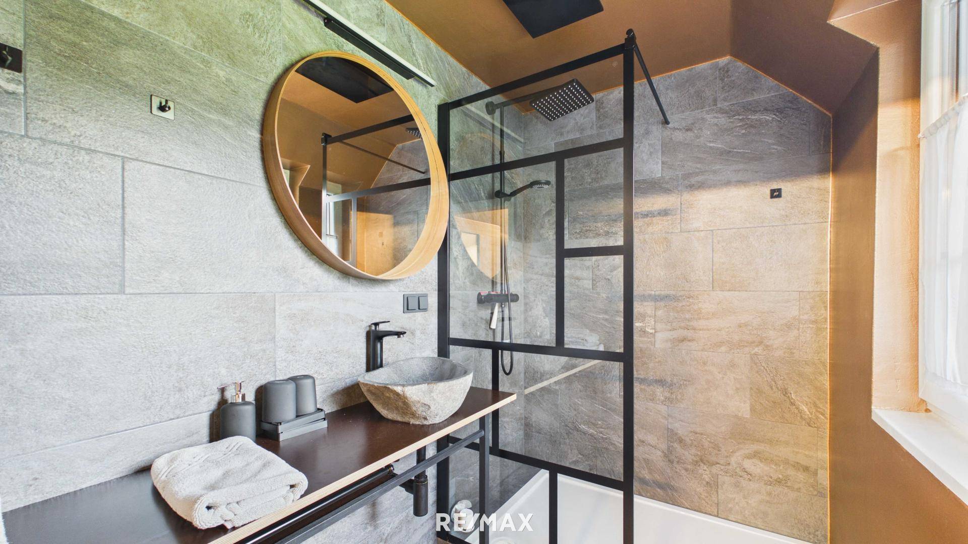 Modernes Badezimmer mit Steinfliesen, runden Spiegel und begehbarer Dusche.