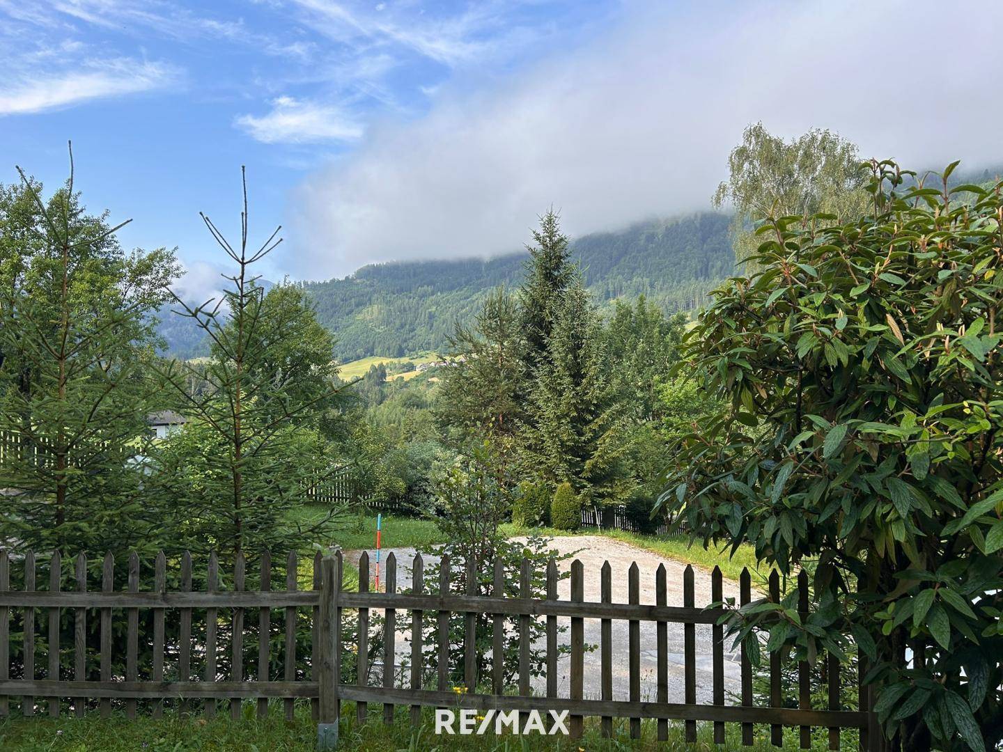 Weitläufiger Blick auf grüne Hügel und bewaldete Berge mit einem Holzzaun im Vordergrund.
