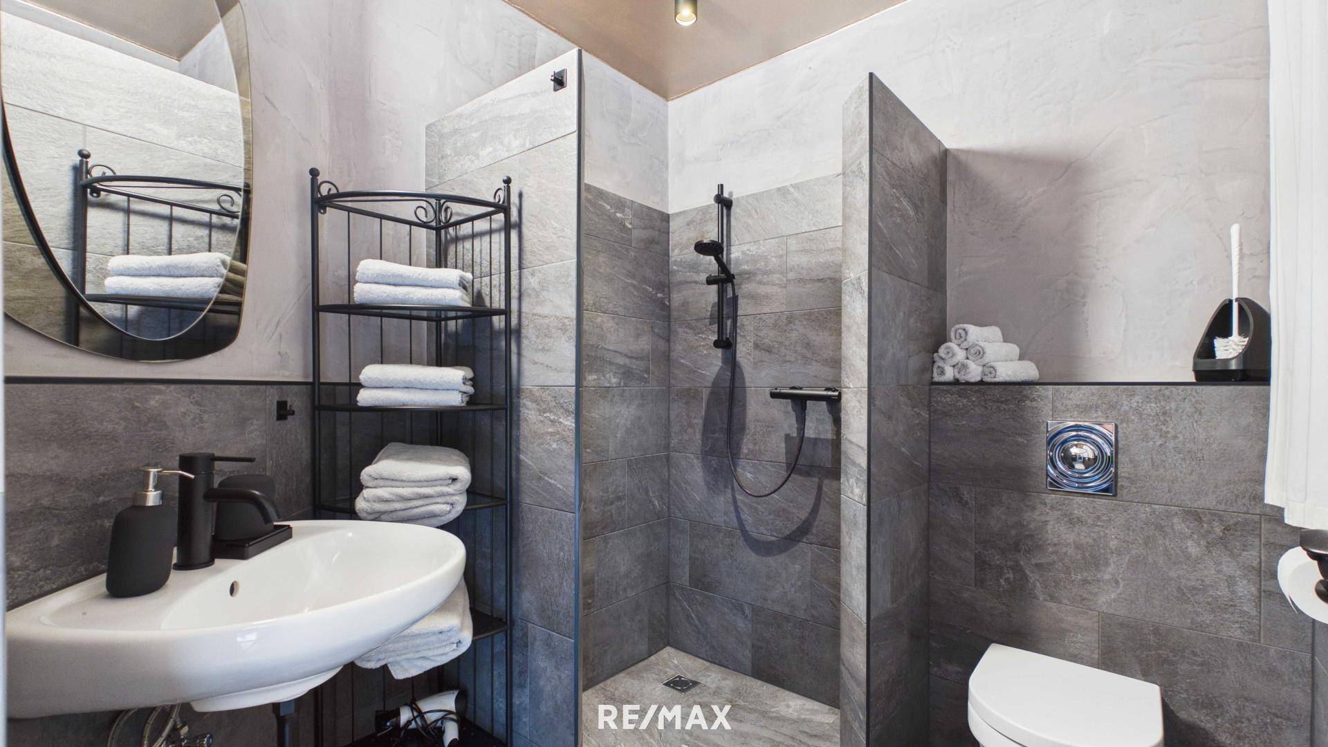 Modernes Badezimmer mit grauen Fliesen, Waschbecken und einer begehbaren Dusche.