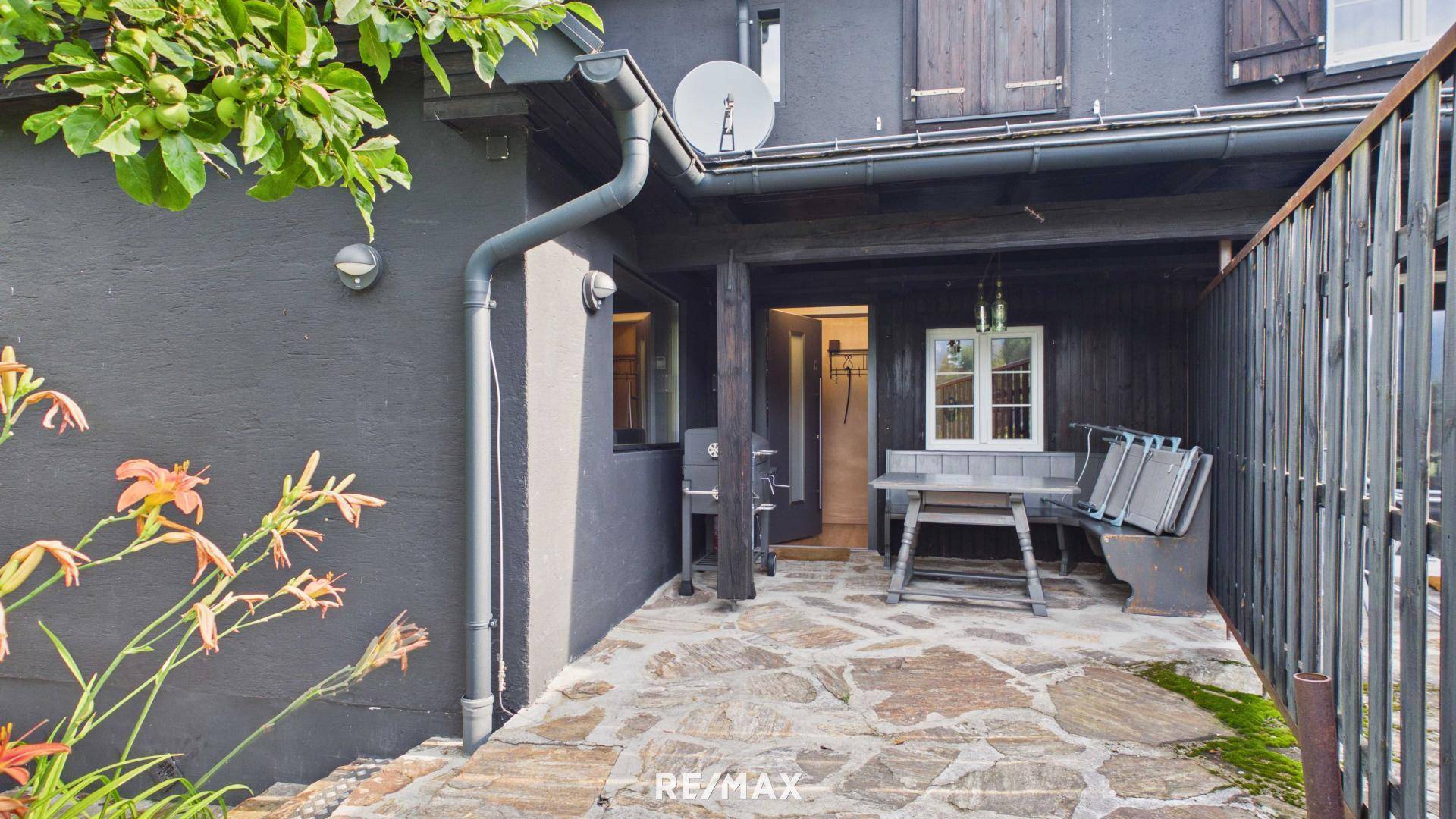 Überdachte Terrasse mit Steinfliesen und rustikalen Holzmöbeln, ideal für Mahlzeiten im Freien.