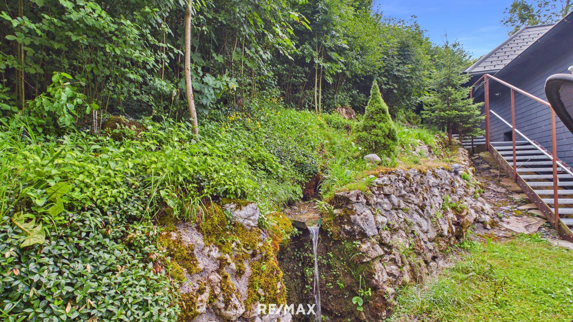 Natürlicher Bachlauf mit Felsen und üppiger Vegetation im Gartenbereich.