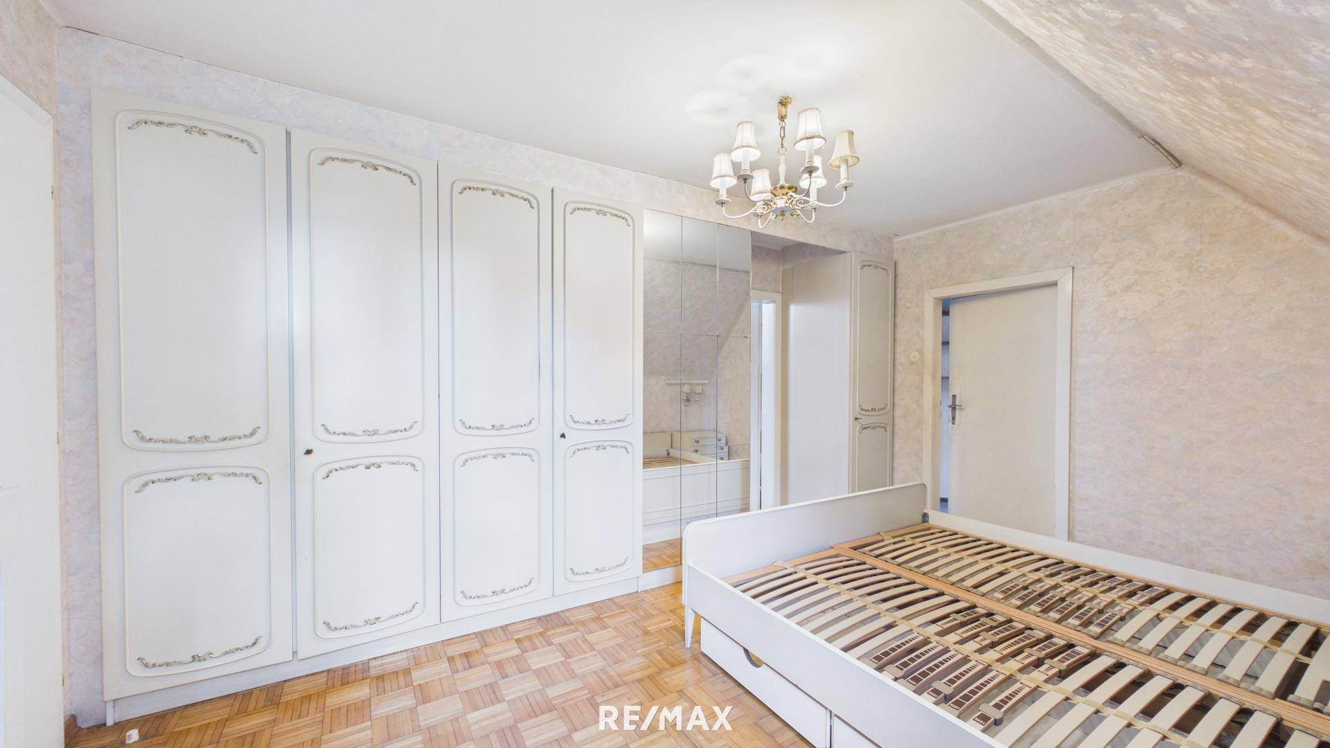 Schlafzimmer mit großem weißen Kleiderschrank, Holzboden und Dachschräge.