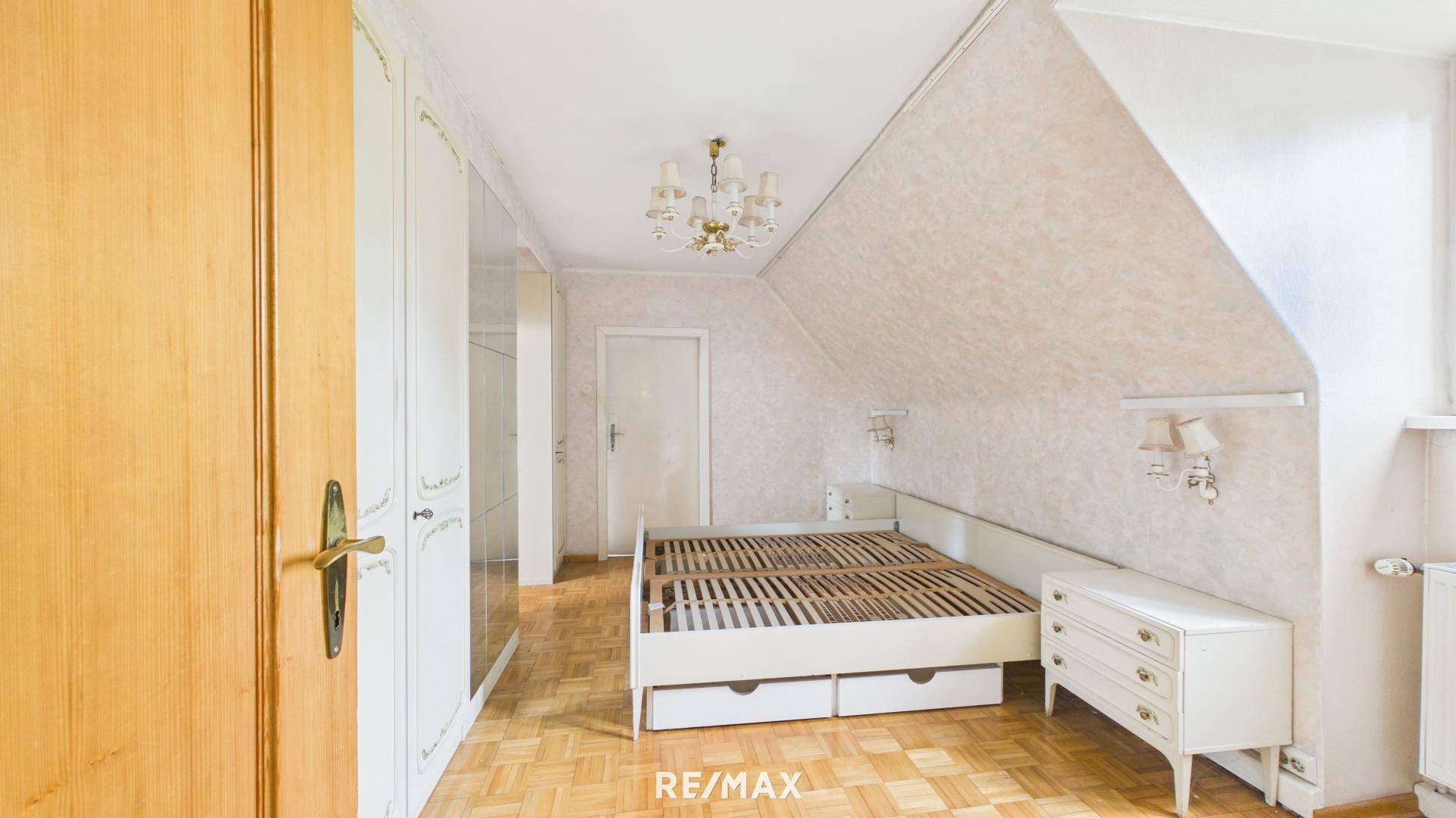 Schlafzimmer im Dachgeschoss mit Parkettboden, Bett und weißen Einbauschränken.