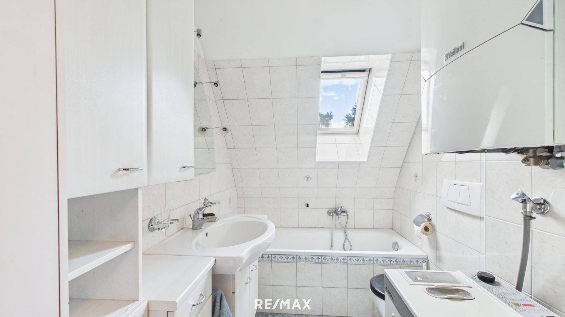 Helles Badezimmer mit weißen Fliesen, Badewanne und Dachfenster, inklusive Gastherme.