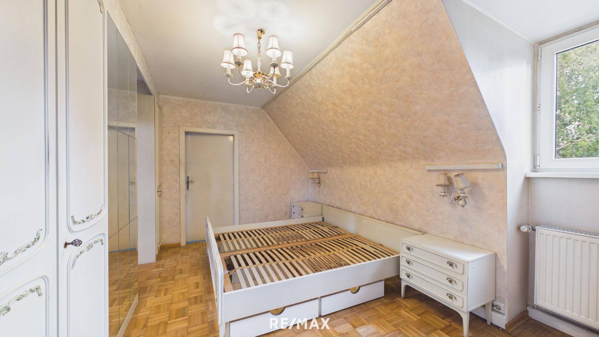 Schlafzimmer mit Parkettboden, Bett, weißen Einbauschränken und Fenster im Dachgeschoss.
