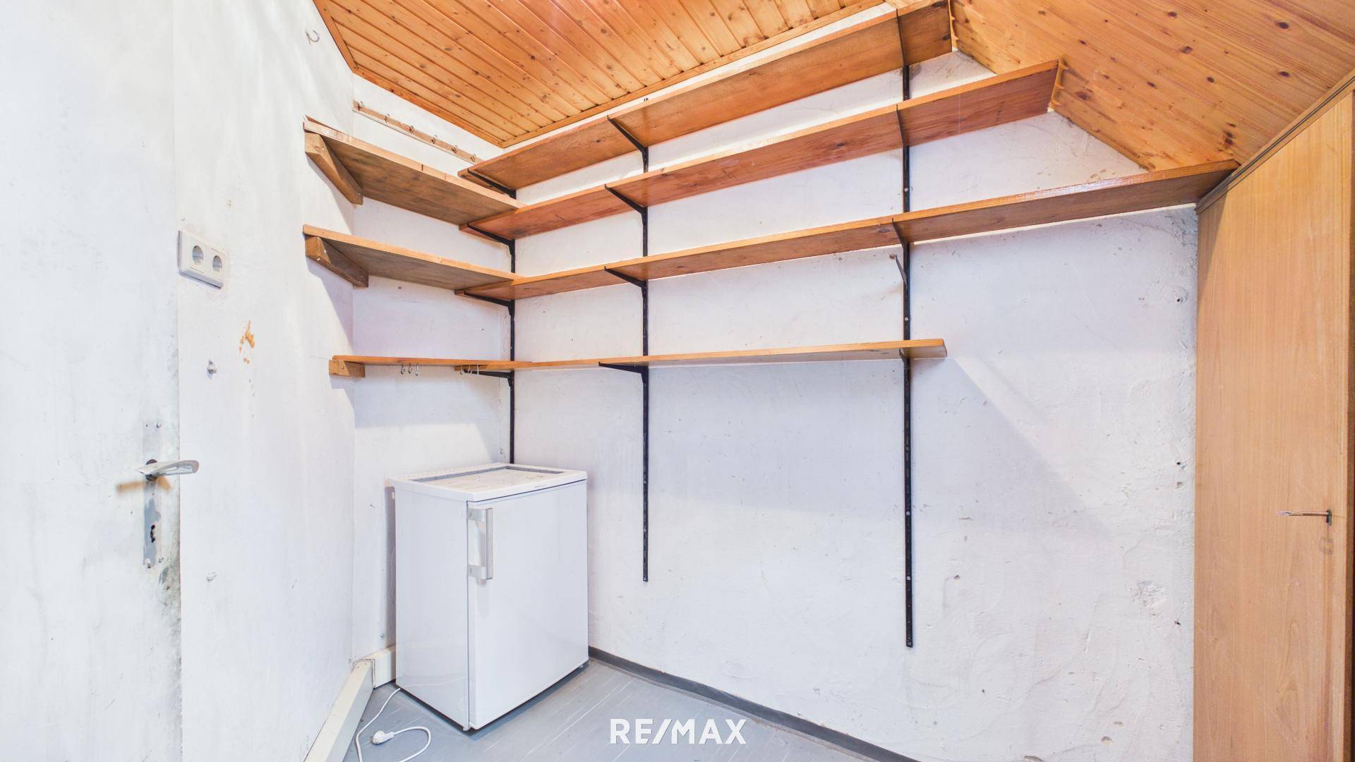 Abstellraum mit Holzdecke, Regalen und kleinem Kühlschrank, bietet zusätzlichen Stauraum.