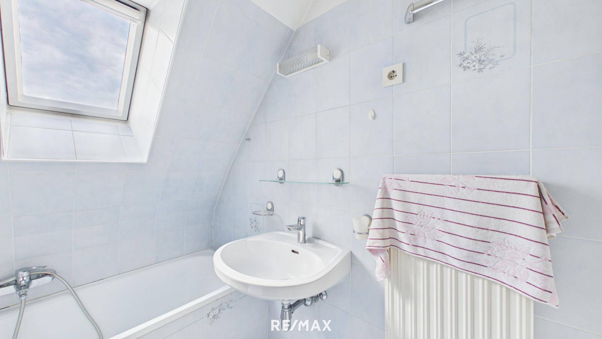 Helles Badezimmer mit Badewanne, Waschbecken und Dachfenster, komplett gefliest.