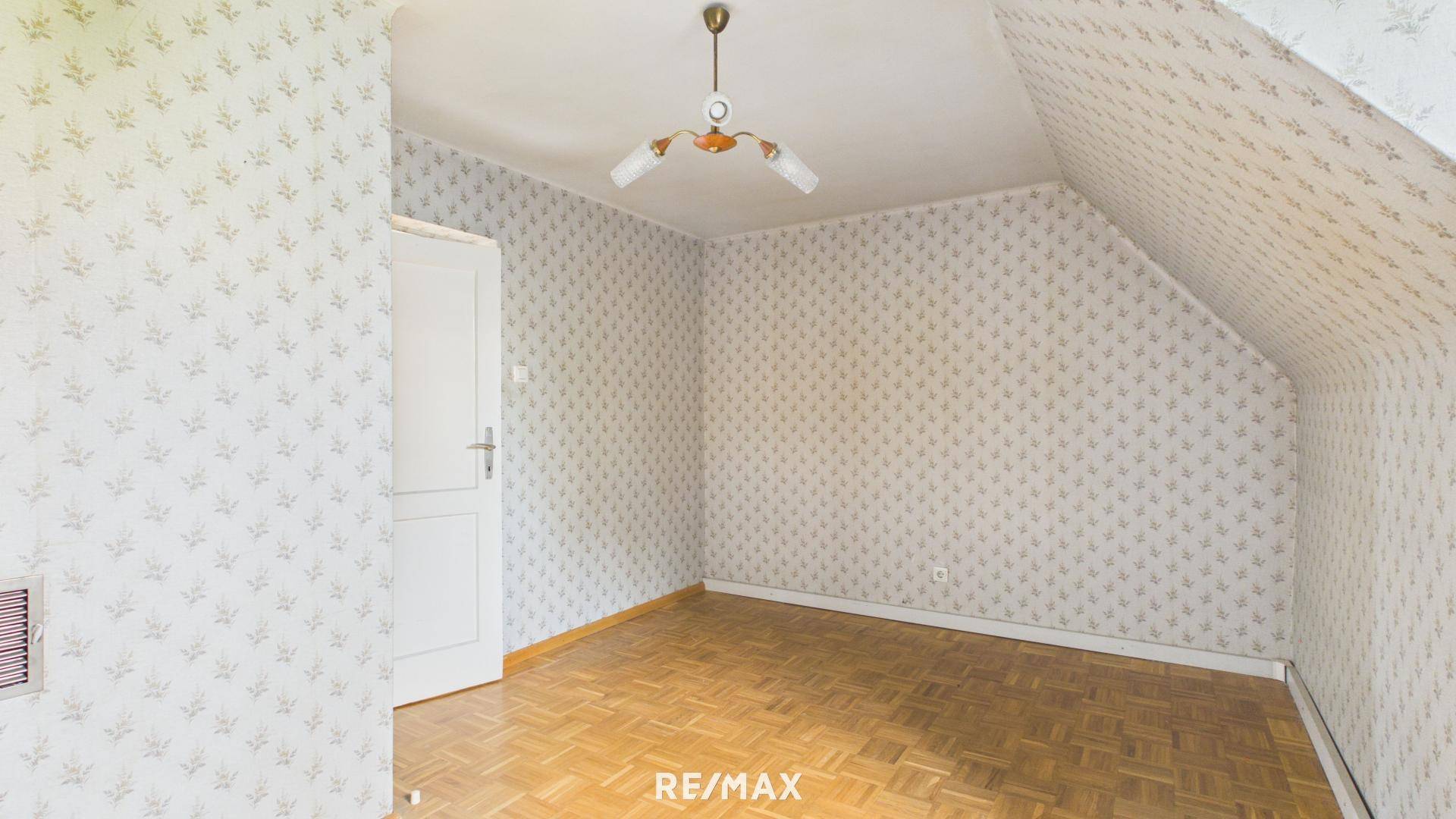 Dachzimmer mit gemusterter Tapete, Holztür und Parkettboden, ideal als Schlaf- oder Arbeitszimmer.