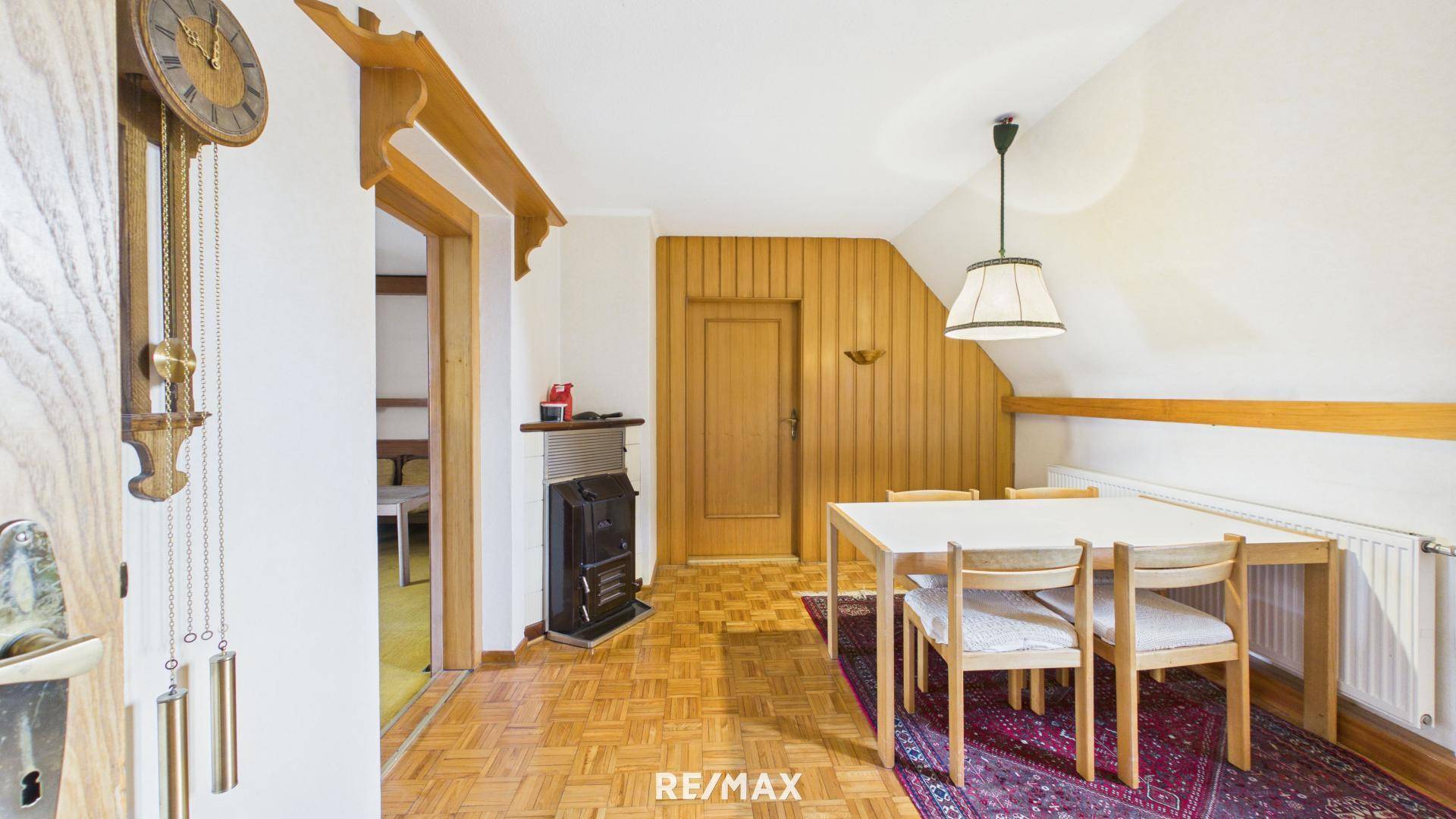 Gemütliches Esszimmer mit Holztisch, Stühlen und einem traditionellen Ofen im Dachgeschoss.