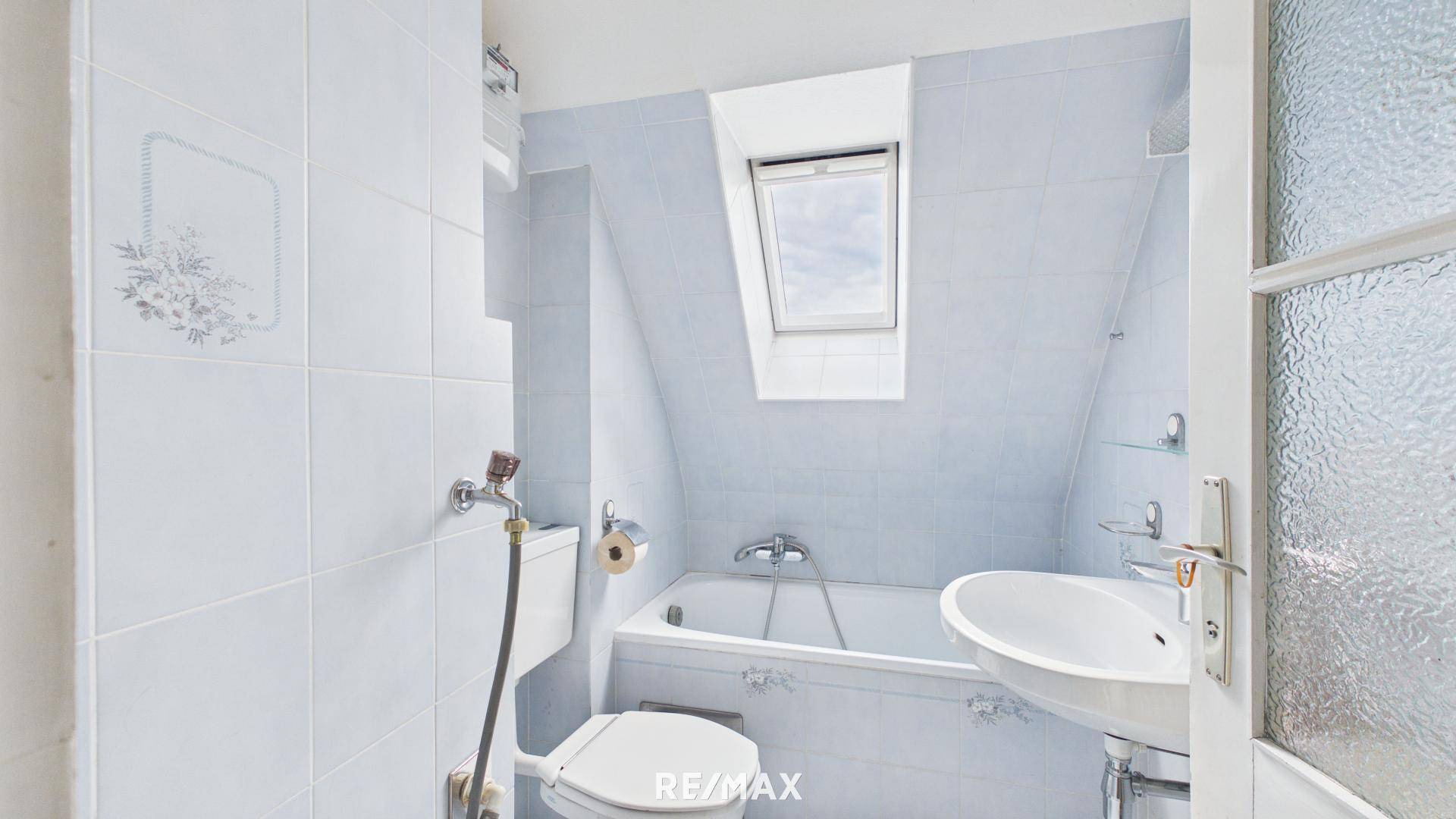 Badezimmer im Dachgeschoss mit hellblauen Fliesen, Badewanne und Dachfenster.